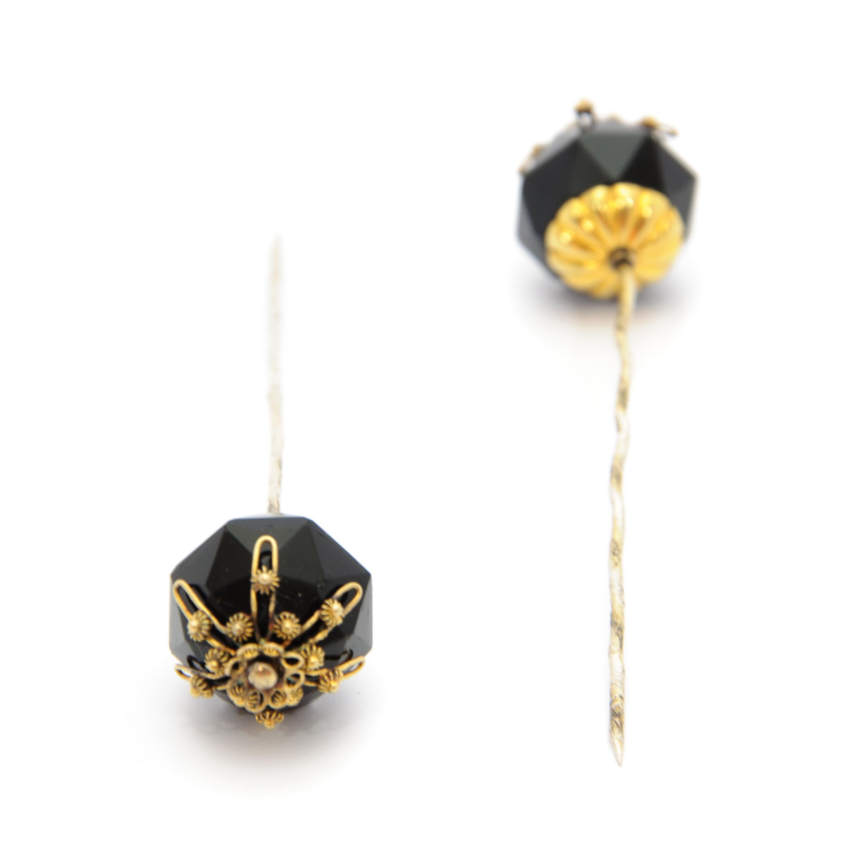 These antique 19th century stick pins are made of black jet and adorned with 14 karat gold cannetille work. The black stone rests on an engraved rosette. The pin itself is gilded and beautifully twisted from top to bottom.

These stick pins
