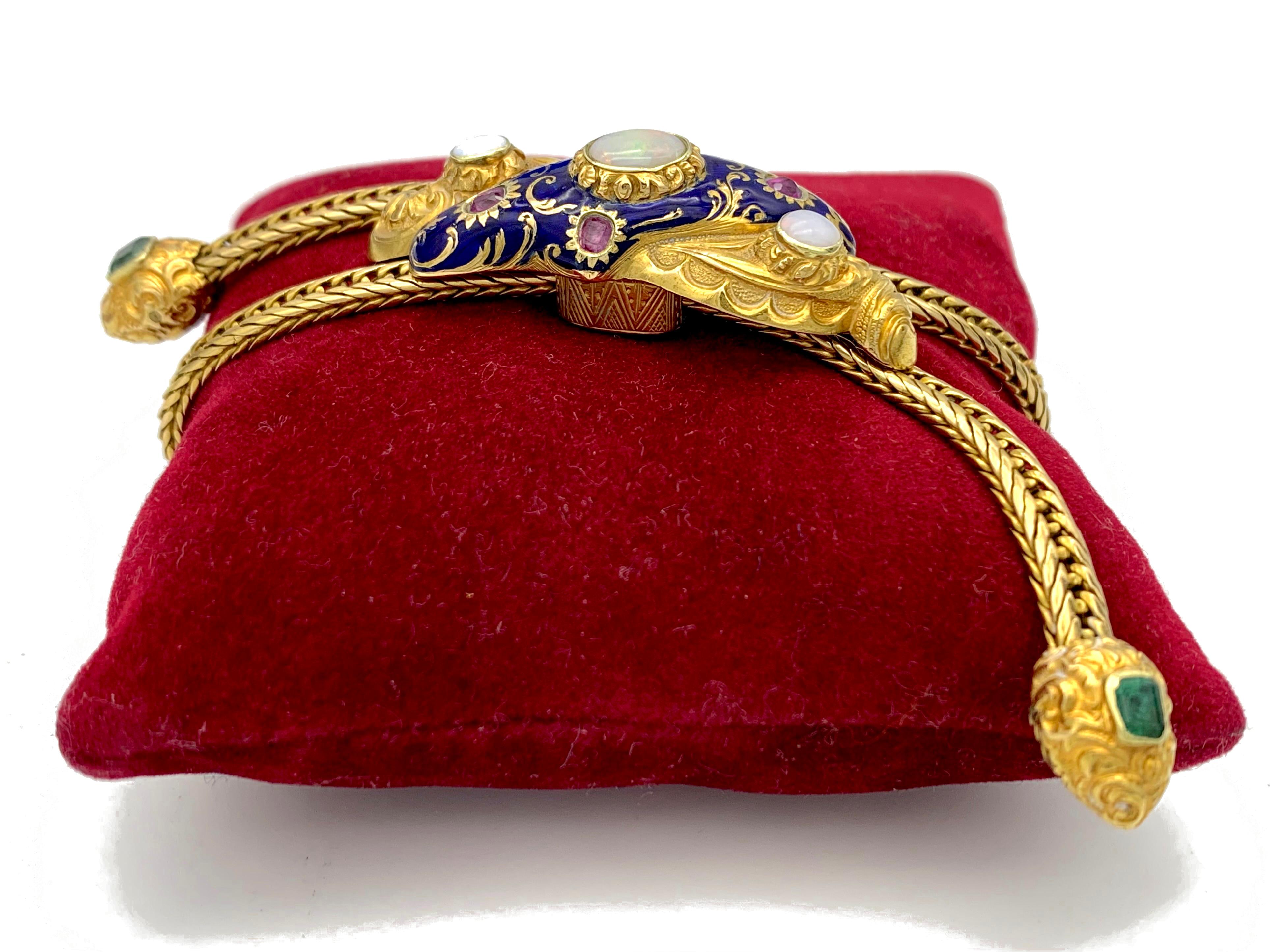 This unusual bracelet features a wonderful navy blue enamelled slide designed as a bow.. The jewel is set with rubies and opals and decorated with acanthus leaves and other foliage. The solid flexible chain terminates into two heart shaped elements
