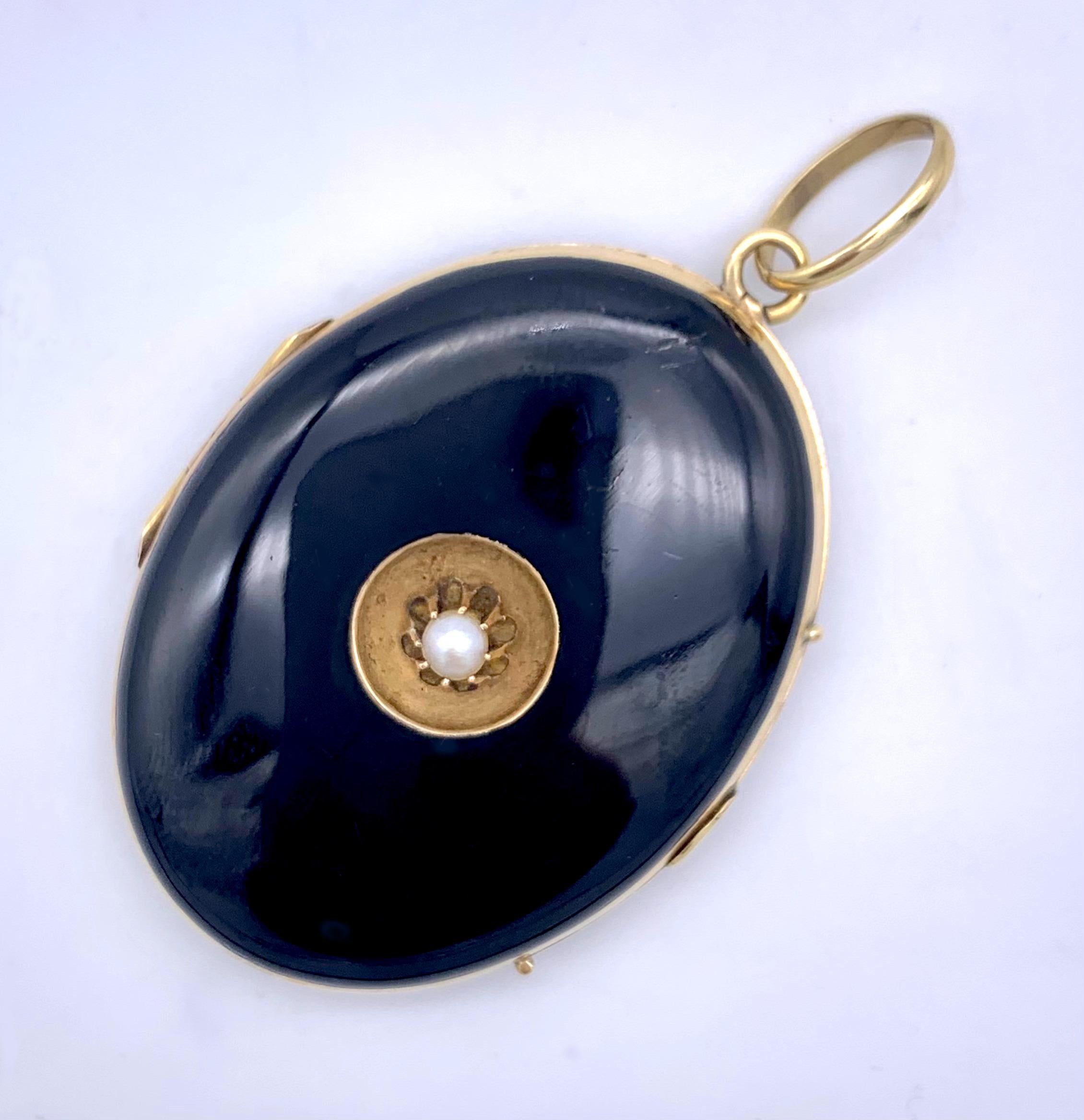 This elegant much loved and worn double sided locket is covered in black enamel. The front is decorated with a claw set natural peal within a matt yellow gold surround. On the inside the locket has retained the oiginal gold frames with their