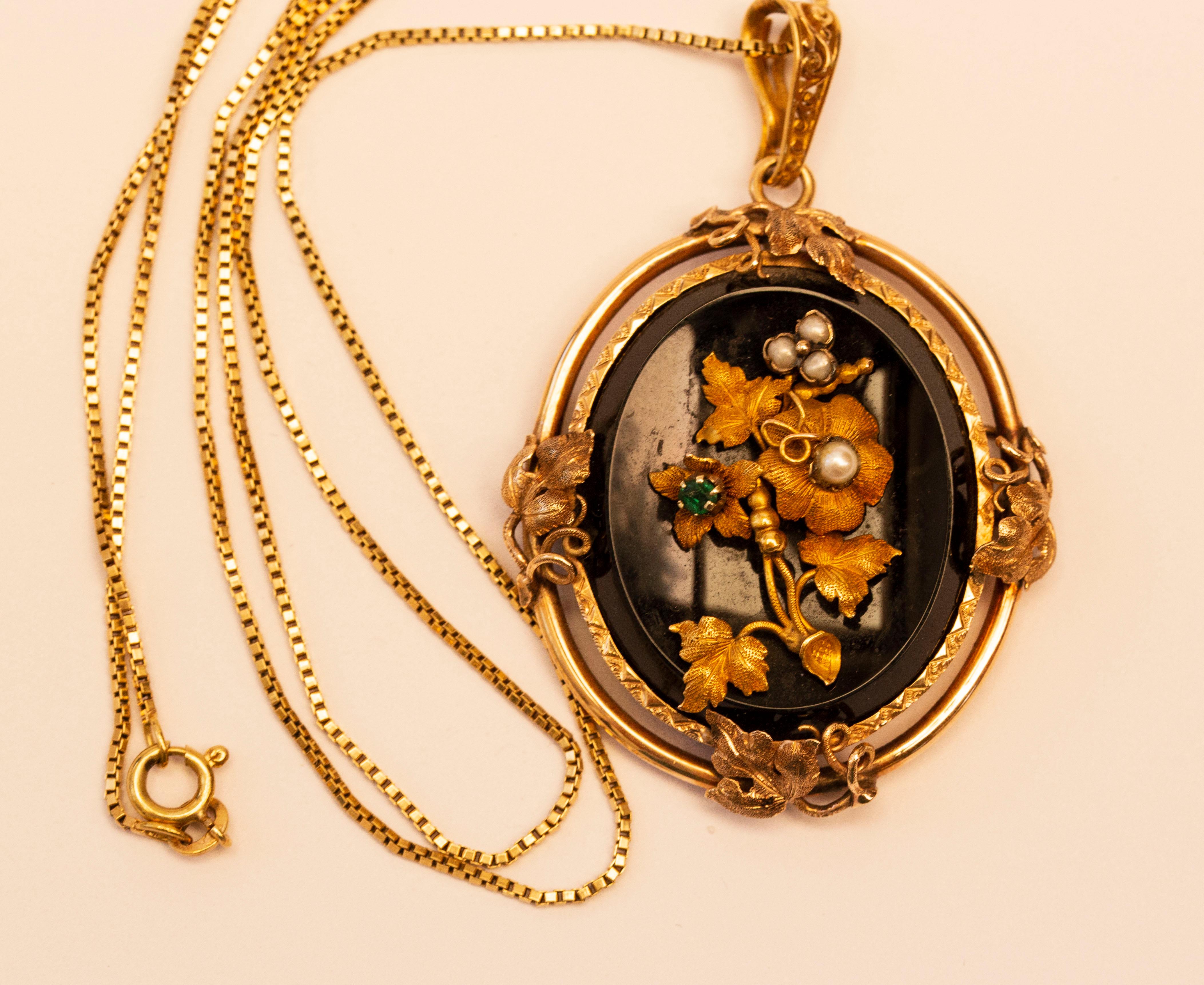 A Victorian antique 14 karat oval onyx pendant with a floral decoration assembled of pearls, emerald, and engraved gold leaves with petals. In the past the pendant was also used a brooch, but the pin to attach it is missing now ( please see the