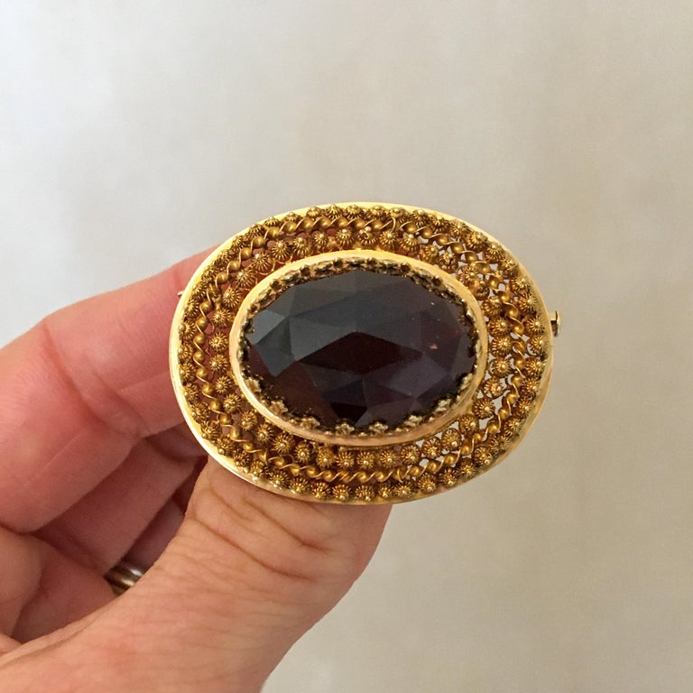 Victorian 14 karat yellow gold oval pin brooch made with fine filigree and set with a large faceted garnet. The garnet is set in a beautifully designed gold frame, surrounded by many small gold knots. Twisted gold thread is placed between the two