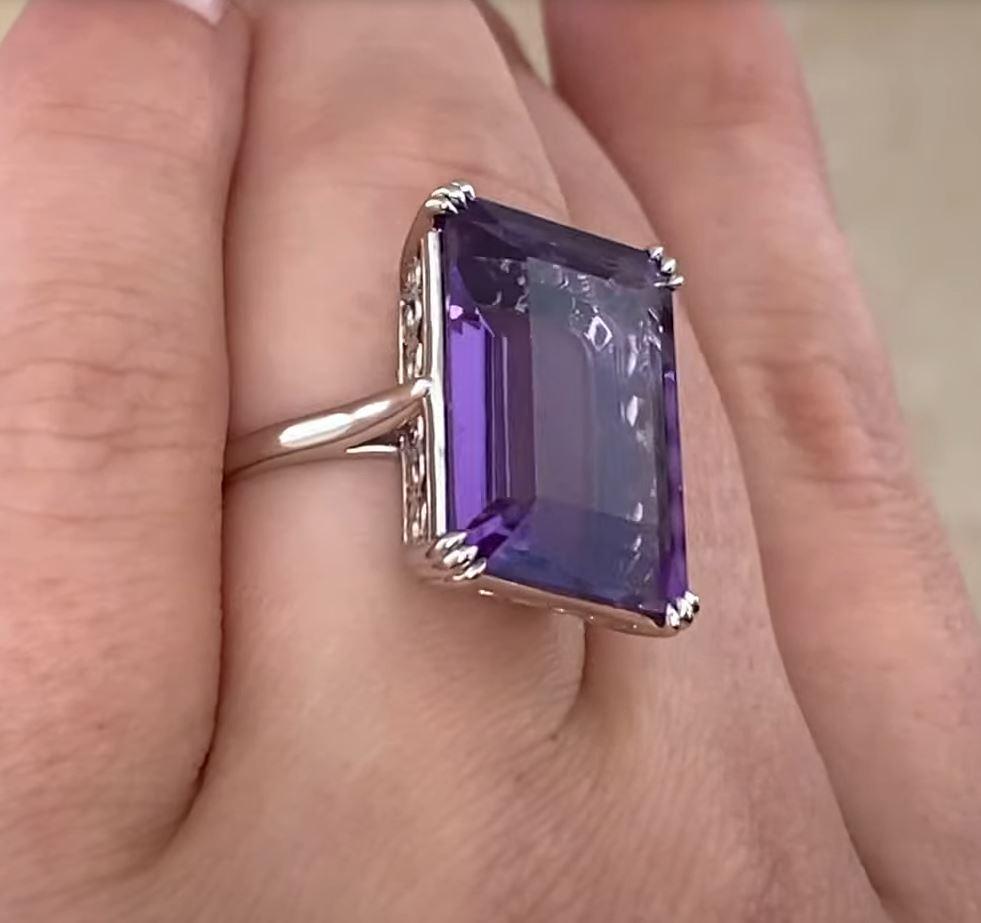 This striking antique ring showcases a stunning emerald-cut amethyst as its centerpiece, weighing an impressive approx. 14.70-carats. The rich, violet hue of the amethyst is complemented by the geometric precision and elegance of its Art Deco