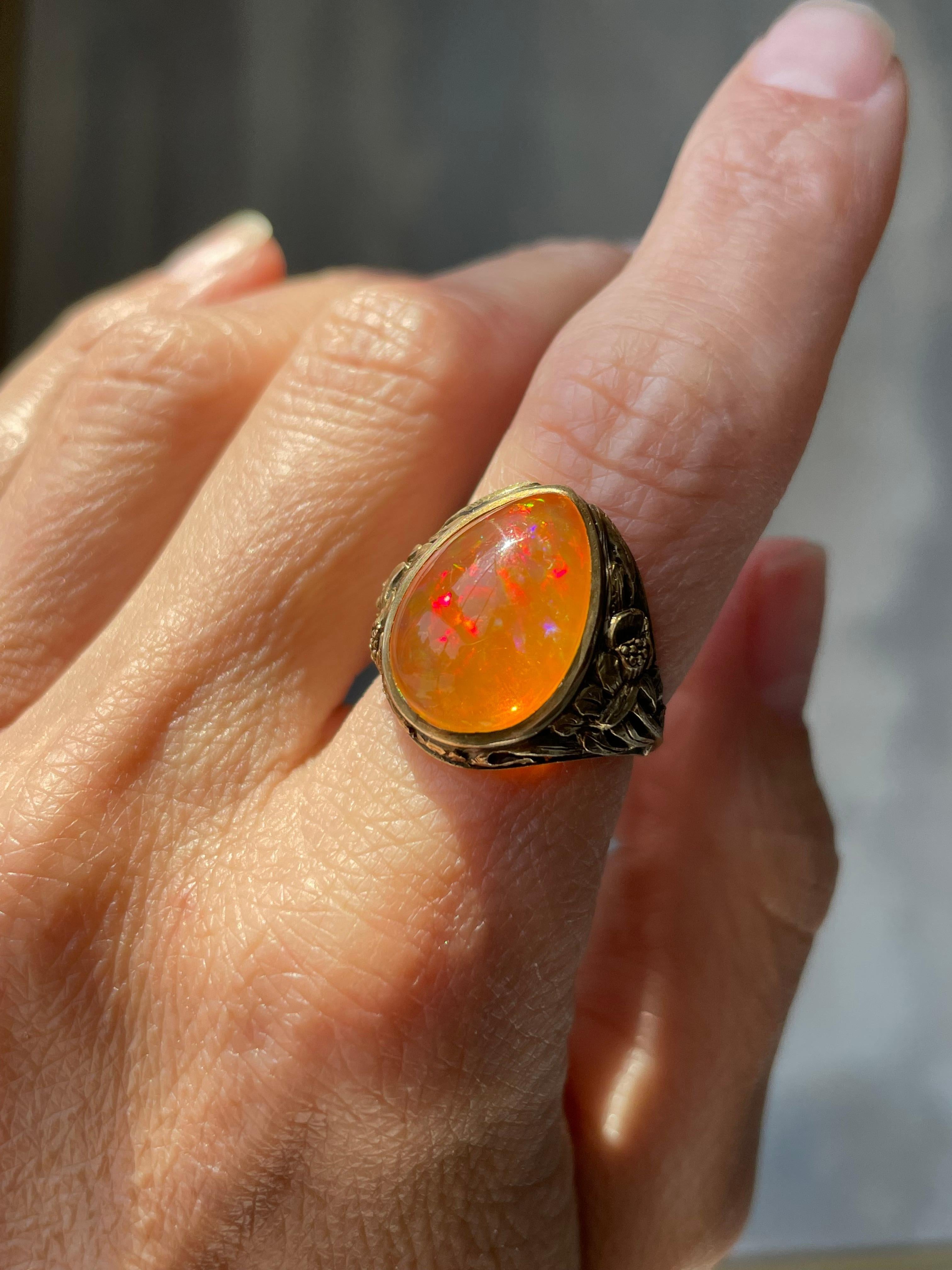 Dating from the early 20th century, this ravishing Art Nouveau ring centers on a glowing Mexican opal filled with confetti-like flashes of bright yellow, vibrant red, brilliant blue and neon green. The opal is perfectly presented in a sculpted 14k