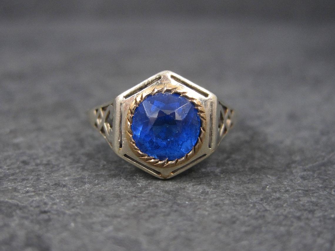 This beautiful antique ring is 14k white gold with a thin line of yellow gold around the stone.

Measurements:
The simulated blue stone is 7mm (apx 1 carat).
The face of the ring measures just shy of 1/2 of an inch.

The ring is a size