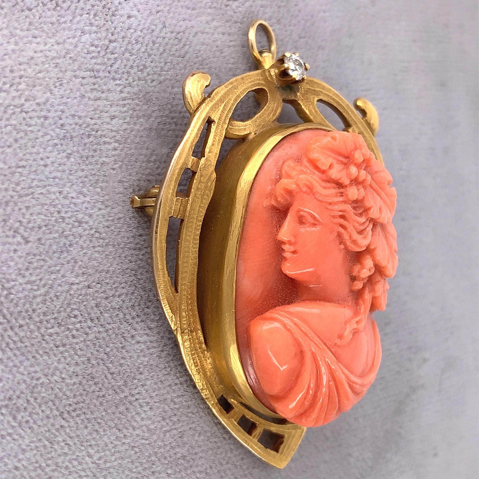 14K yellow gold Art Nouveau coral cameo pin featuring a large portrait of a woman with grapes and grape leaves in her hair. The crisp detailed cameo measures about 28mm x 20mm. Accenting the Art Nouveau cast setting is a small European cut diamond