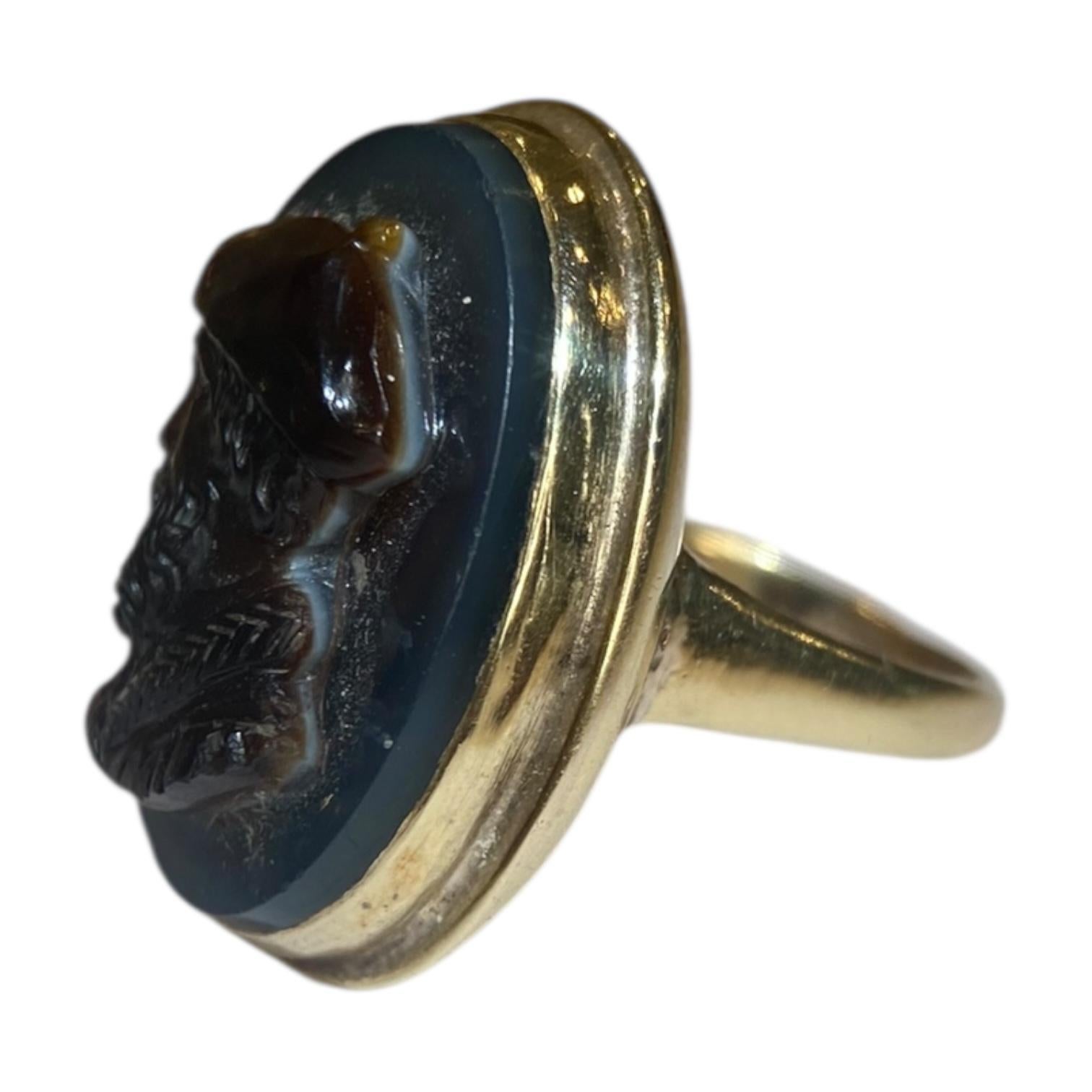 Fabriquée en or jaune 14 carats, cette bague est ornée d'un camée ovale en agate sculpté à la main. Le design/One présente le profil détaillé d'un homme, ce qui donne de la profondeur et du caractère à la pièce. 
Dimensions : 23.5 mm L x 18.5 mm L.