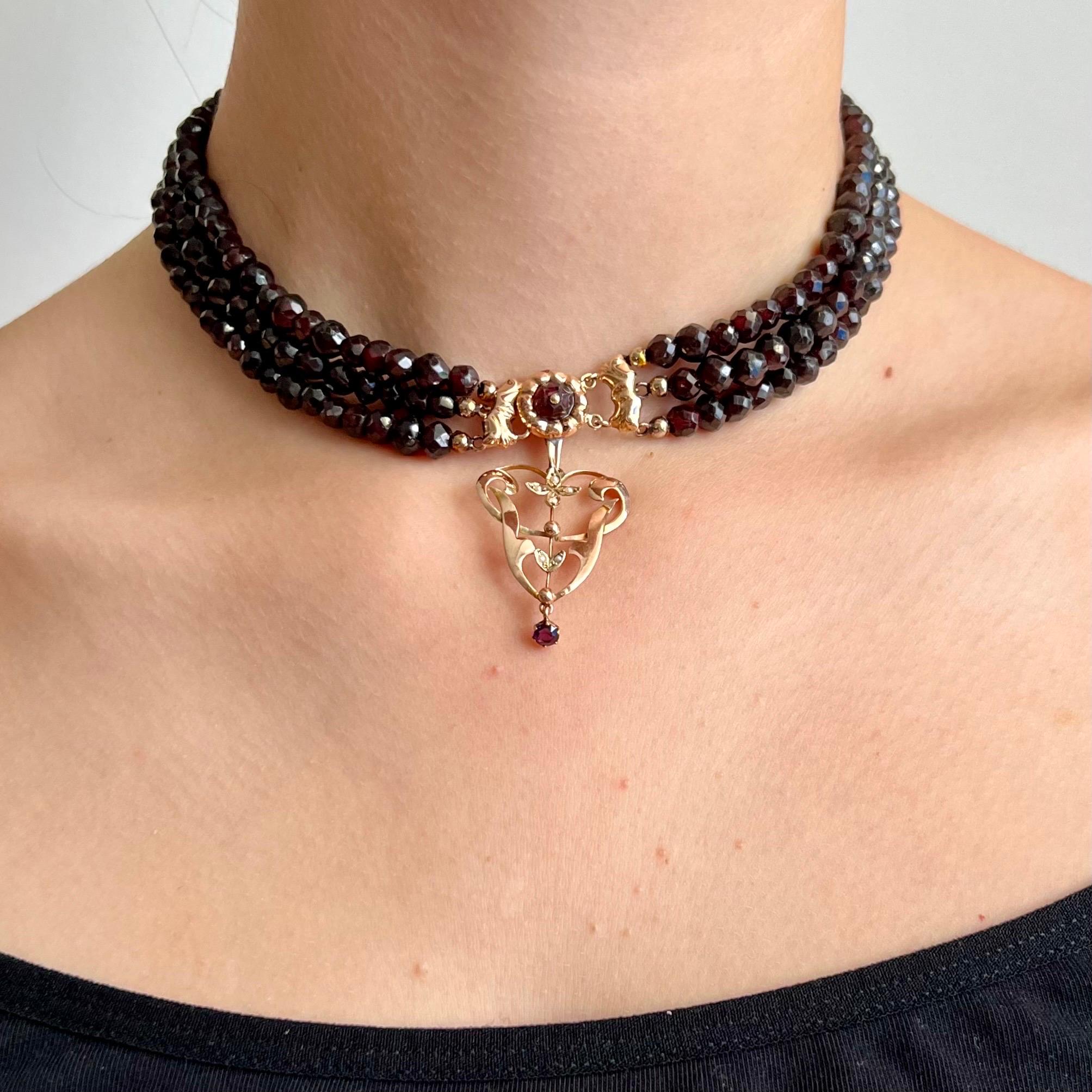 An antique late 19th century garnet necklace set with a 14 karat gold worked clasp. The necklace consists of three strands strung with faceted garnet stones. The gold repousse clasp is round shaped and set with a garnet. Below this round repousse