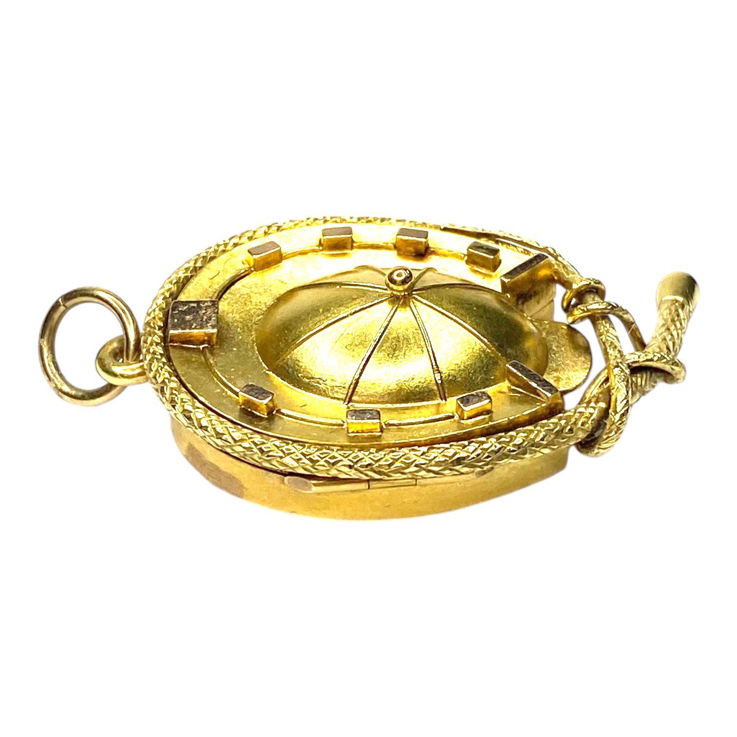 Early 20th Century pendant, crafted in 14k rose gold on the back and yellow gold on the front. The front features a jockey cap encircled by a horseshoe motif, detailed with a textured whip. The back side of the locket has light scratches and small