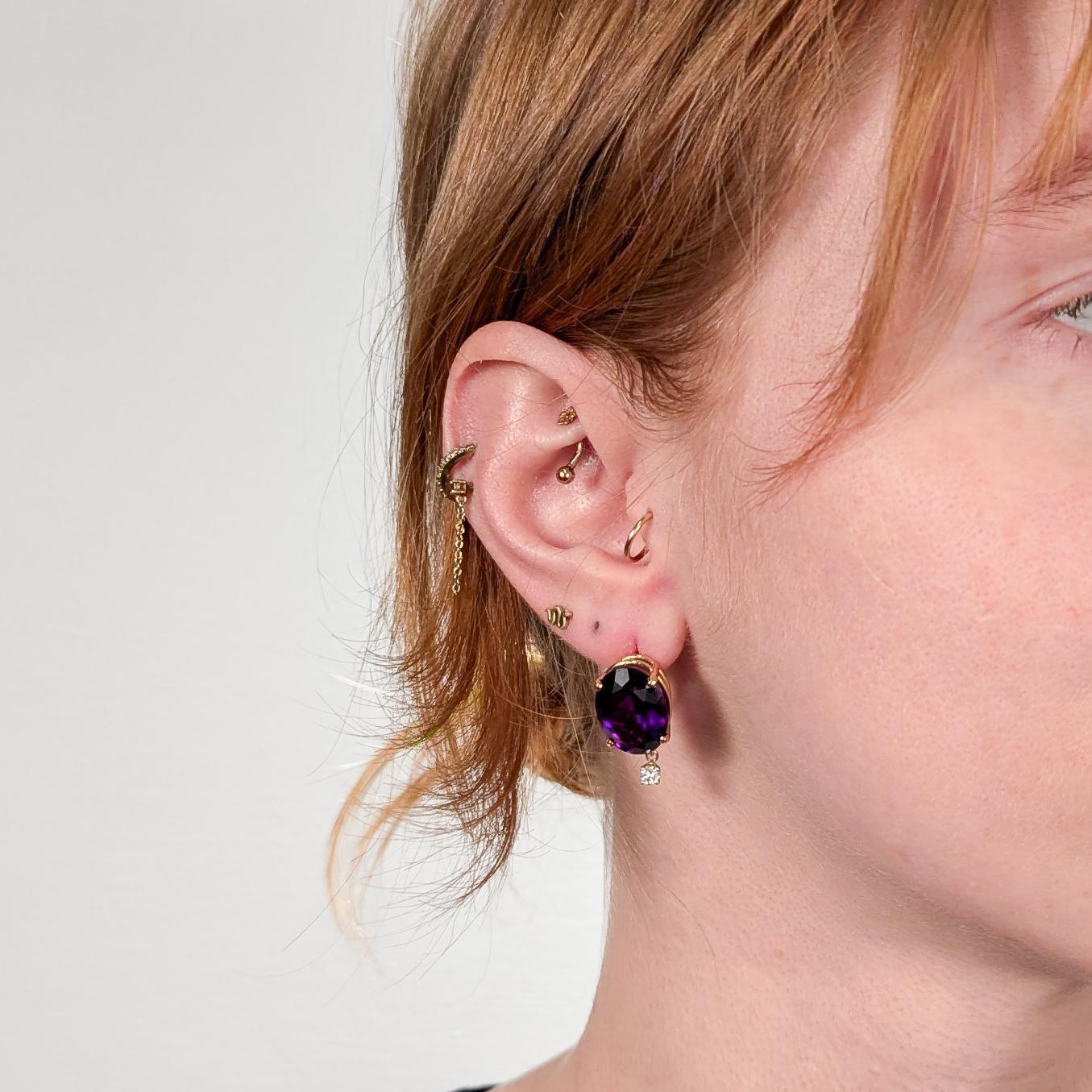 A fine pair of gold, amethyst, and diamond drop earrings.

In 14 karat yellow gold.

Each with oval cut amethyst gemstones in a basket setting with a round brilliant cut diamond drop.

Set with omega clip backs for extra security.

Stamped 14 to the