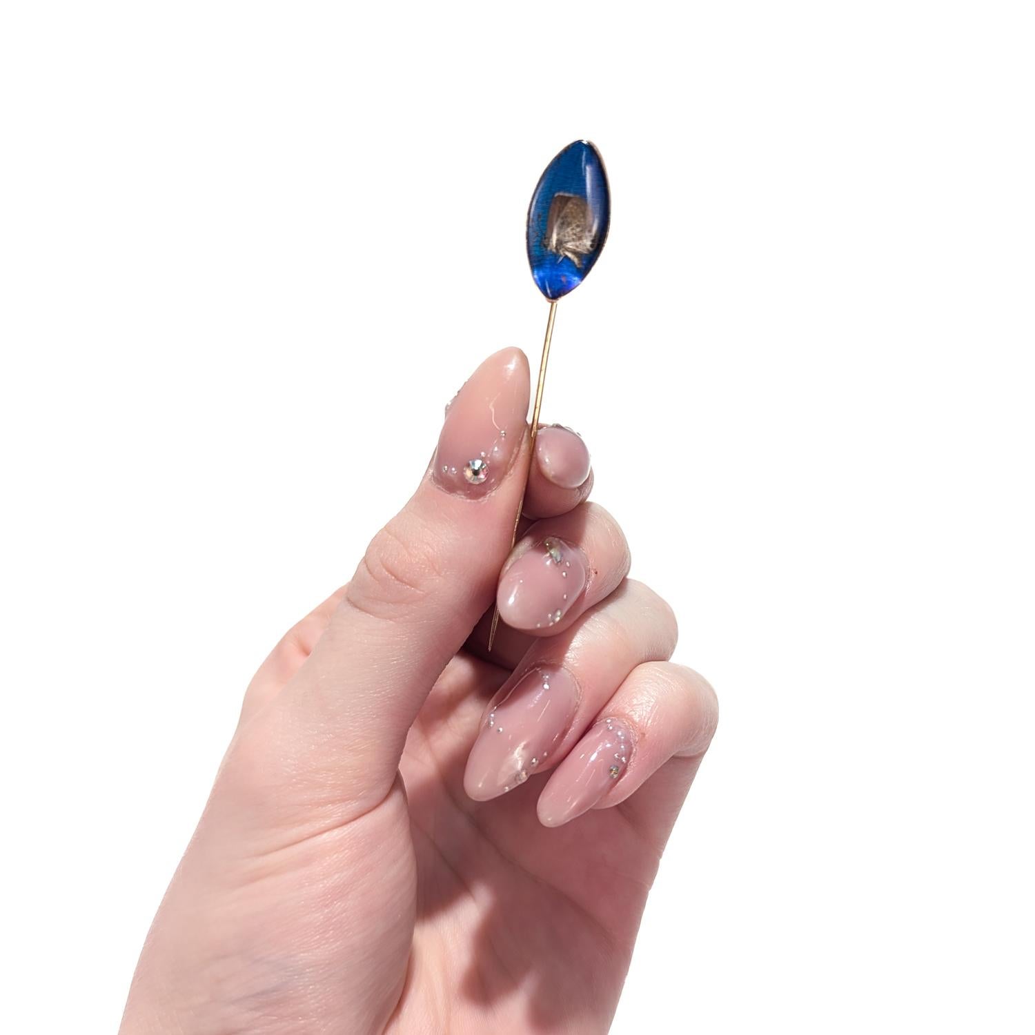A fine antique gold & real butterfly wing stickpin.

In 14 karat yellow gold.

With a very small brown butterfly mounted on a brilliant blue real morpho butterfly wing under an oval crystal cabochon.

Marked to reverse of the bezel for 14k.

Simply