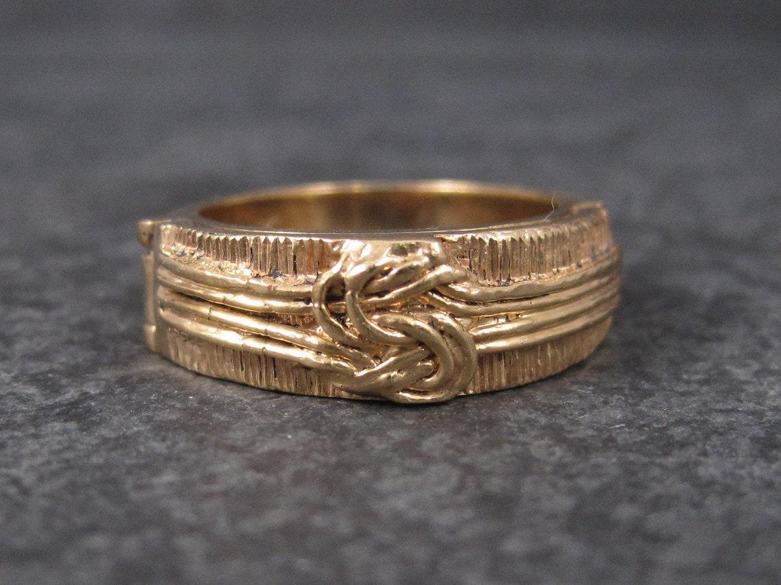 This gorgeous antique love knot ring is 14k yellow gold.

It features a hinged compartment in which one can have a secret message engraved.
This compartment originally would have held plaited hair but since there is no evidence of that, its likely