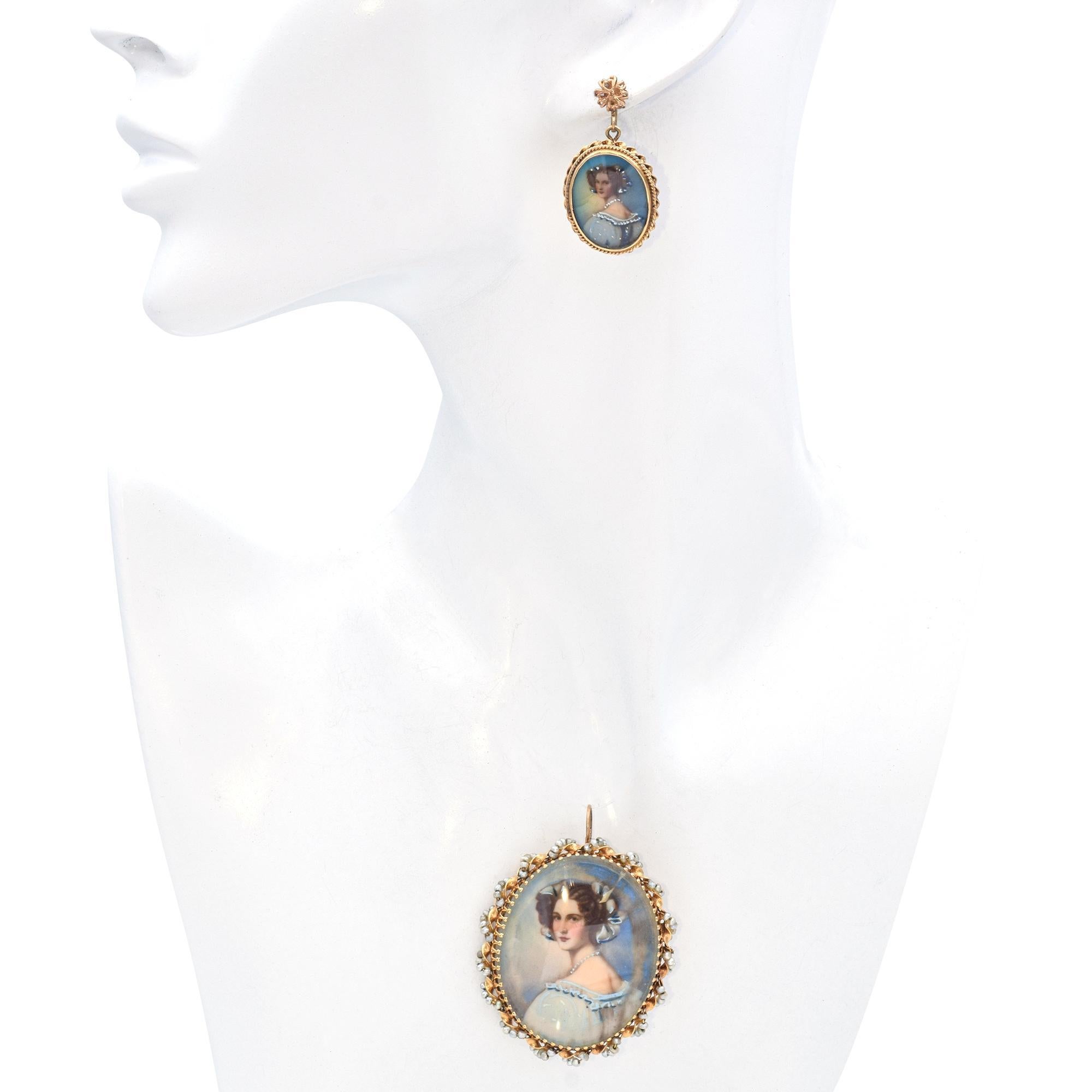 A stunning jewelry set featuring a brooch and matching earrings. Crafted in 14k yellow gold, the set showcases exquisite miniature portraits encased in ornate frames. The brooch is adorned with delicate pearls, enhancing its elegance and charm. The