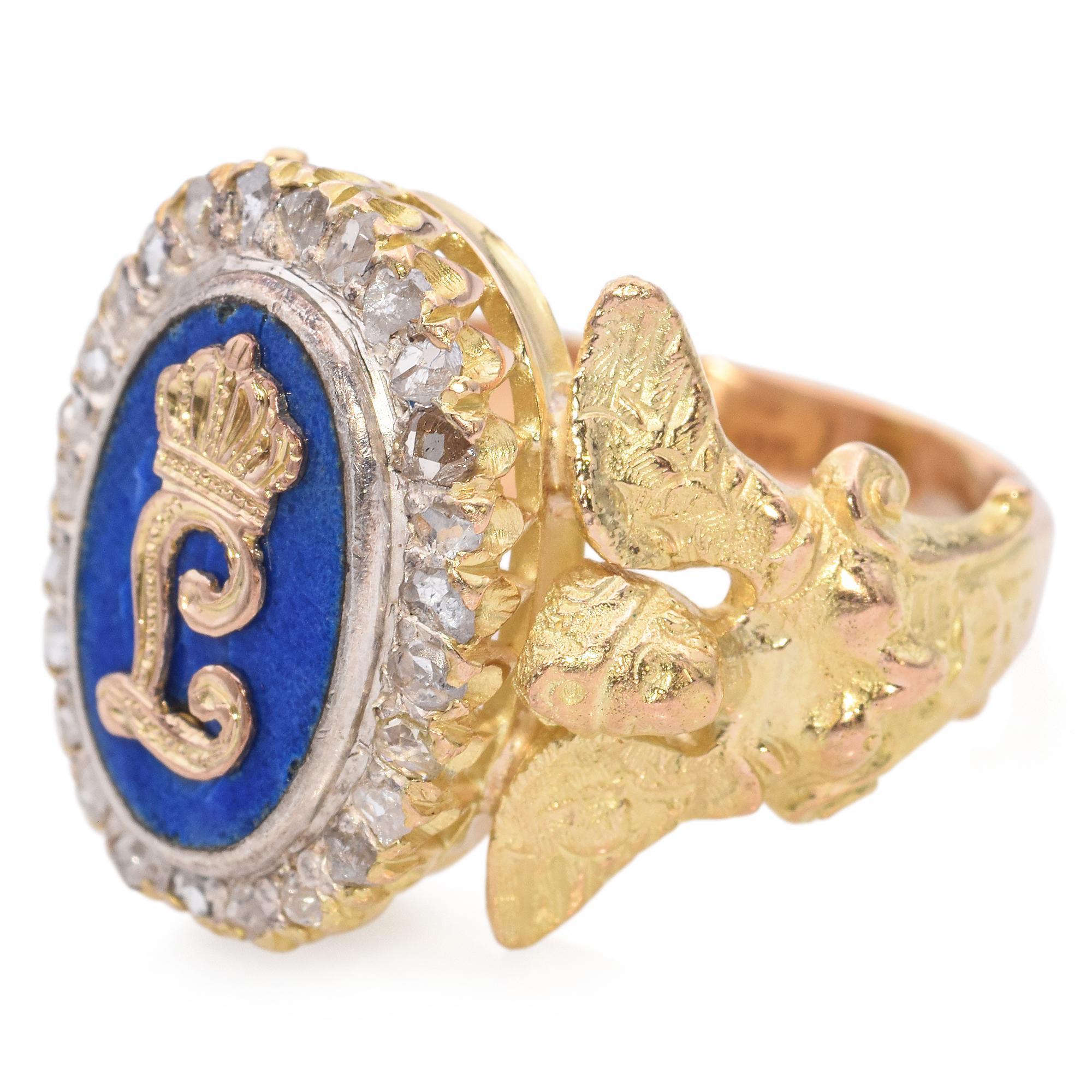 C. Late 19th Century

This Victorian signet ring is crafted in 16K gold. It features a central blue enamel oval adorned with a gold monogram and crown motif, surrounded by a halo of white rose-cut diamonds.The diamonds are set in a delicate border