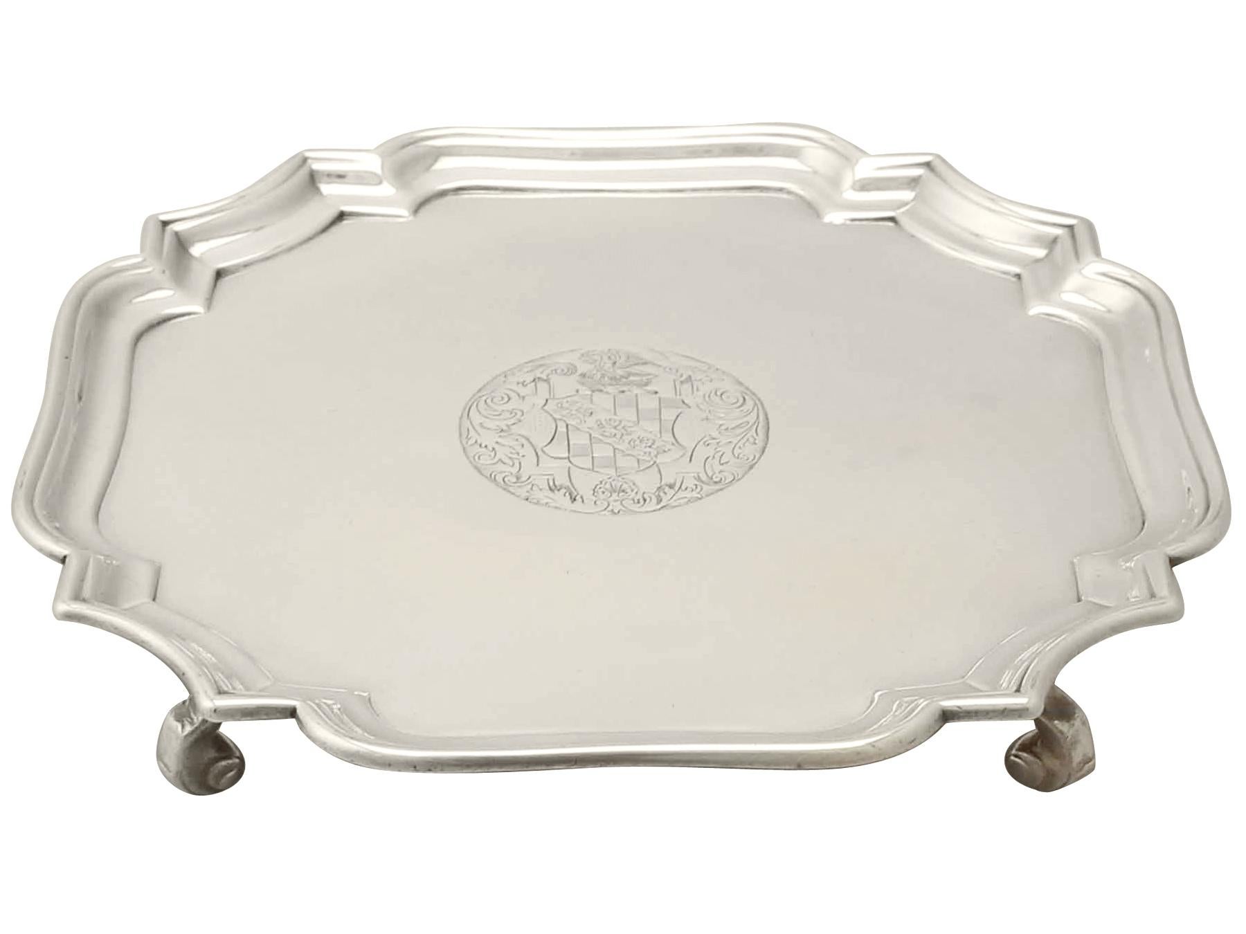 This fine antique sterling silver salver has a plain rounded square form with shaped corners.

The surface of this silver salver is plain and embellished with a circular cartouche incorporating a scrolling leaf bordered contemporary bright cut