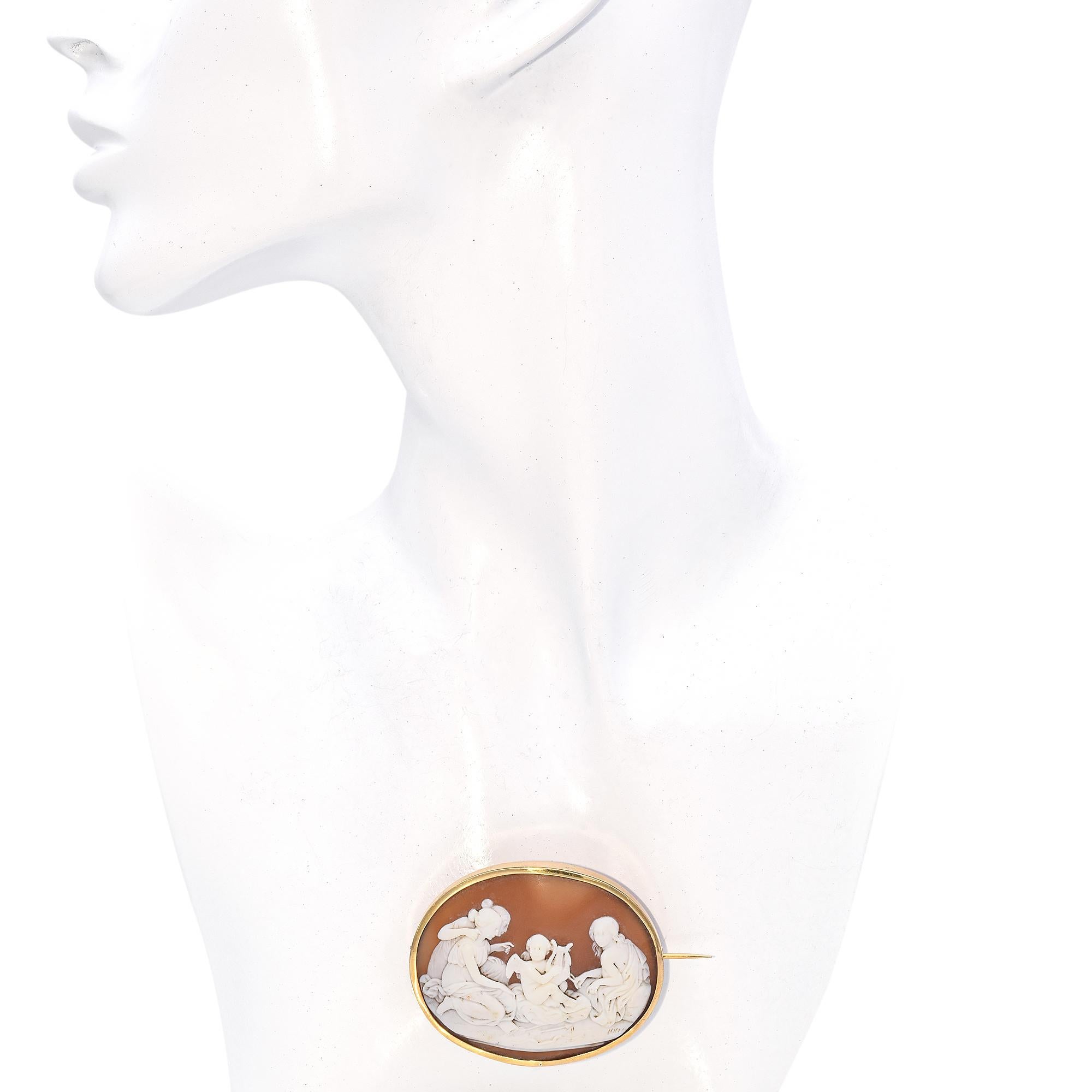 This exquisite piece is crafted in yellow gold, featuring an intricately carved relief.
The design showcases three women and a cherub. The cameo is set within an oval frame, highlighting the contrast between the scene and the warm
