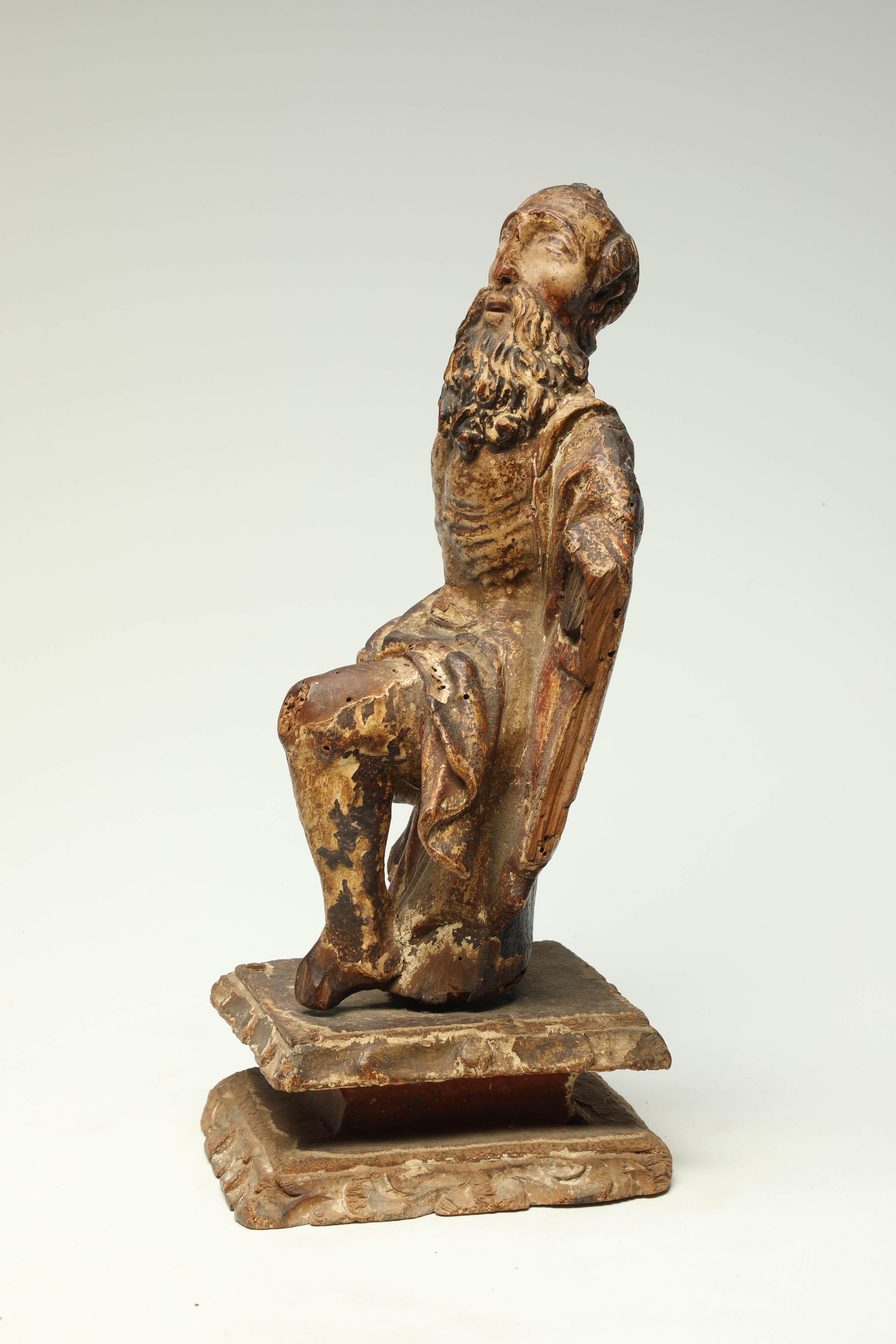 Antico frammento di figura di santo seduto in legno intagliato del XVII-XVIII secolo con barba. Forse anche prima. Resti di pittura o pigmenti in più strati.

Mancano le braccia e una gamba, vecchi danni al naso e ad altre aree. Montato su una base