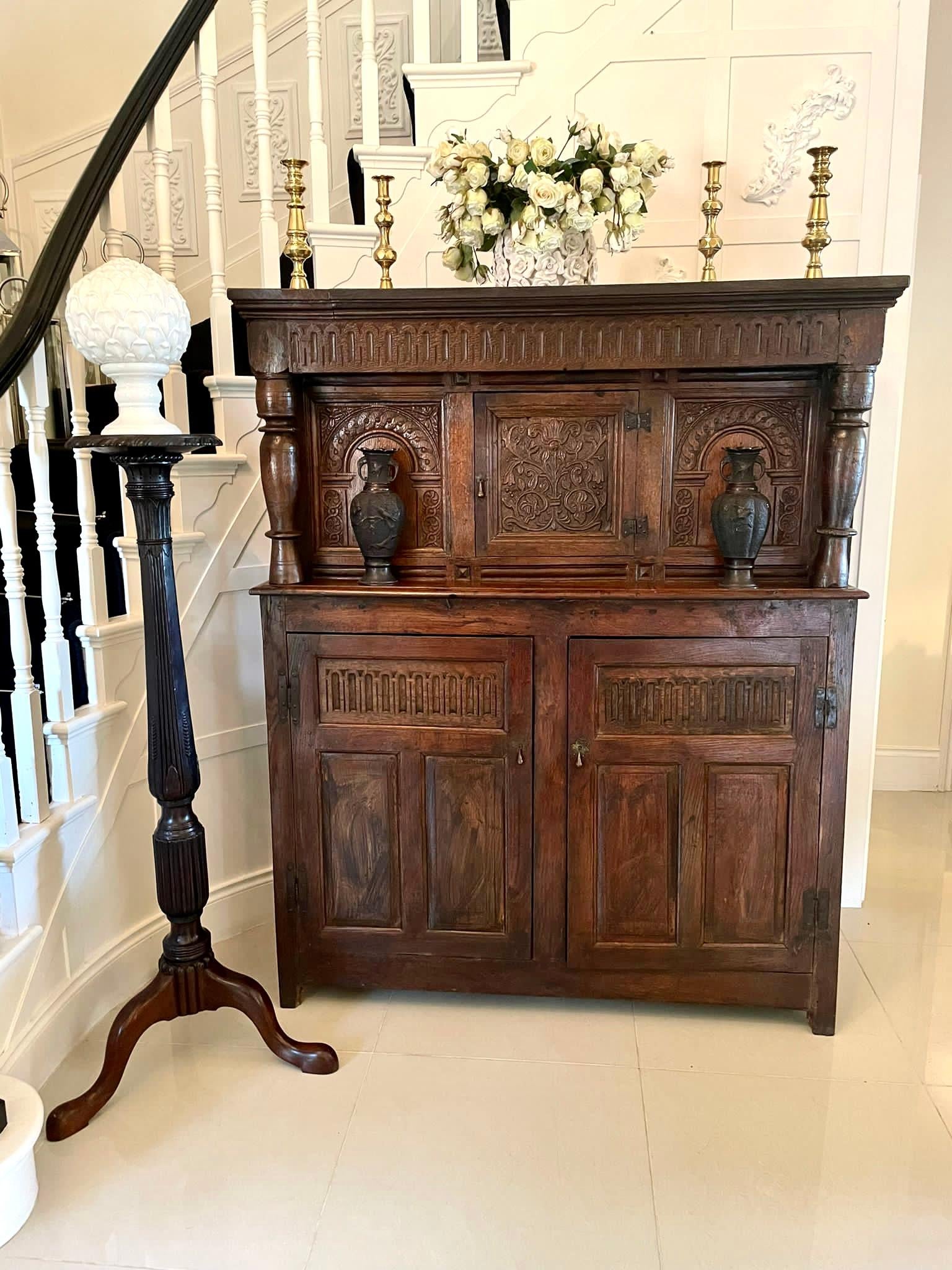 Antique 17th century antique carved oak court cupboard having a splendid shaped cornice, carved oak frieze above a quality carved centre door with iron hinges flanked by two carved panels and a pair of turned oak columns. The base boasts a pair of