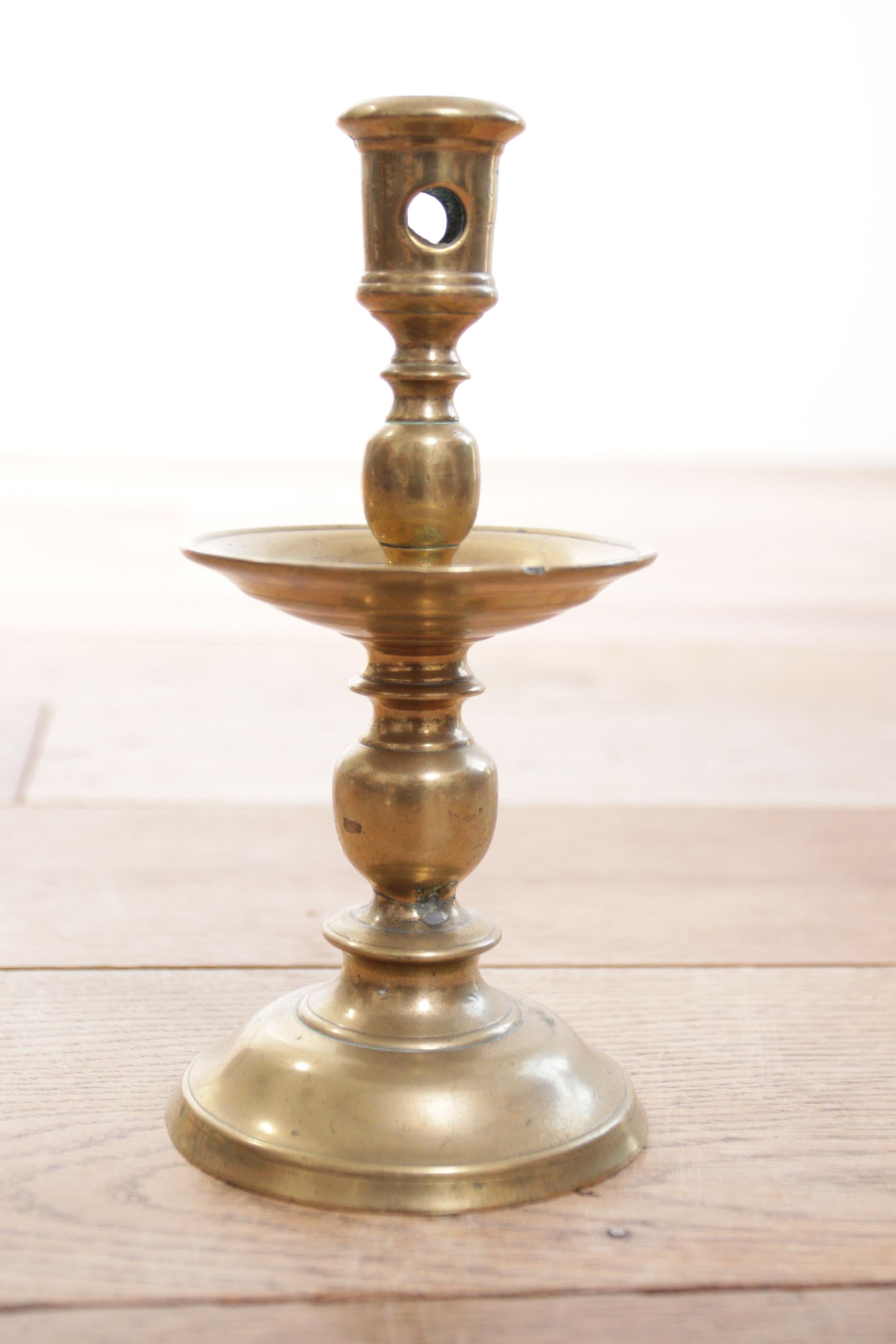 This ‘collar’ candlestick of turned brass dates from about 1650 and was made in the Netherlands. It has a foot in a flattened bell shape and a circular drip pan around the centre.
It was a supremely practical design being sufficiently heavy to sit