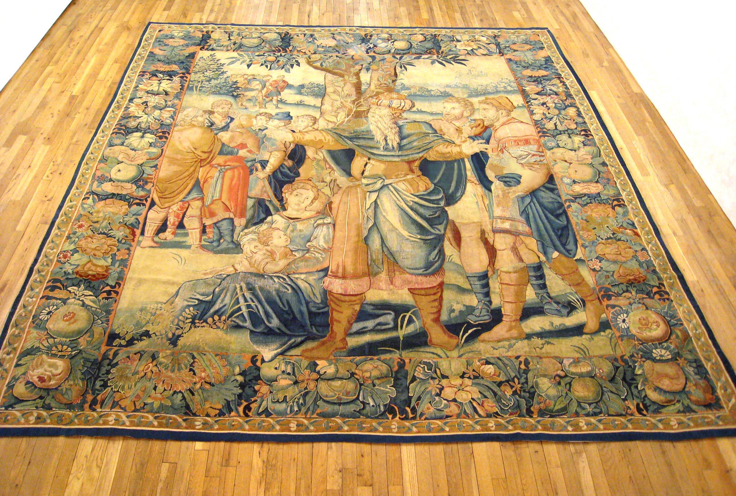An antique 17th century Brussels Old Testament Biblical tapestry, size 11 'H x 10'10 W, featuring Isaac with his sons, Jacob and Esau, and other figures nearby. Enclosed within an elaborate foliate border. Wool with silk inlay. Linen backing. Very