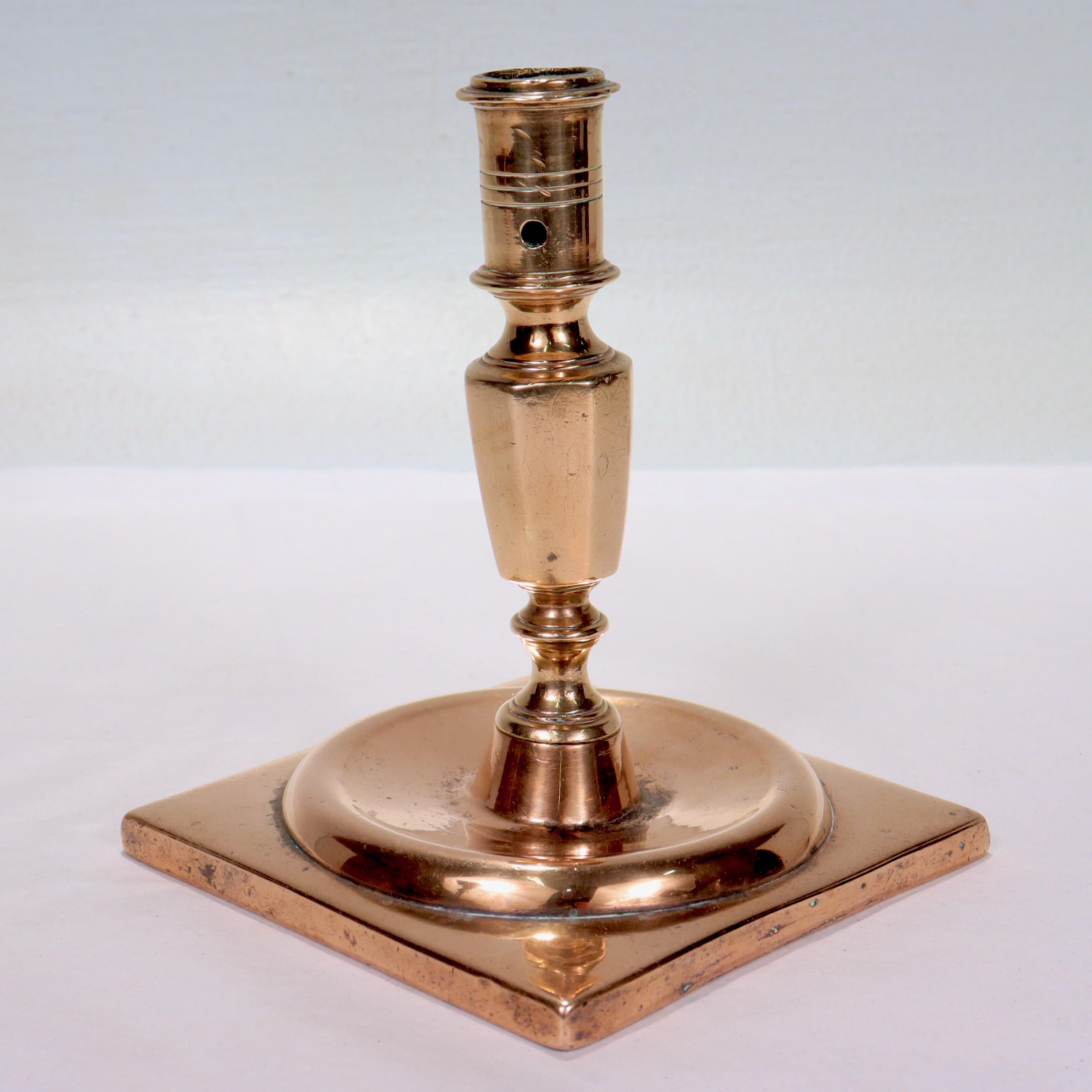A fine antique bronze candlestick

Dating from the end of the 17th Century.

Likely Dutch or English.

With a wide square base supporting a tapered, faceted stem & cylindrical candle cup with a wax. The candlestick is secured to its base by