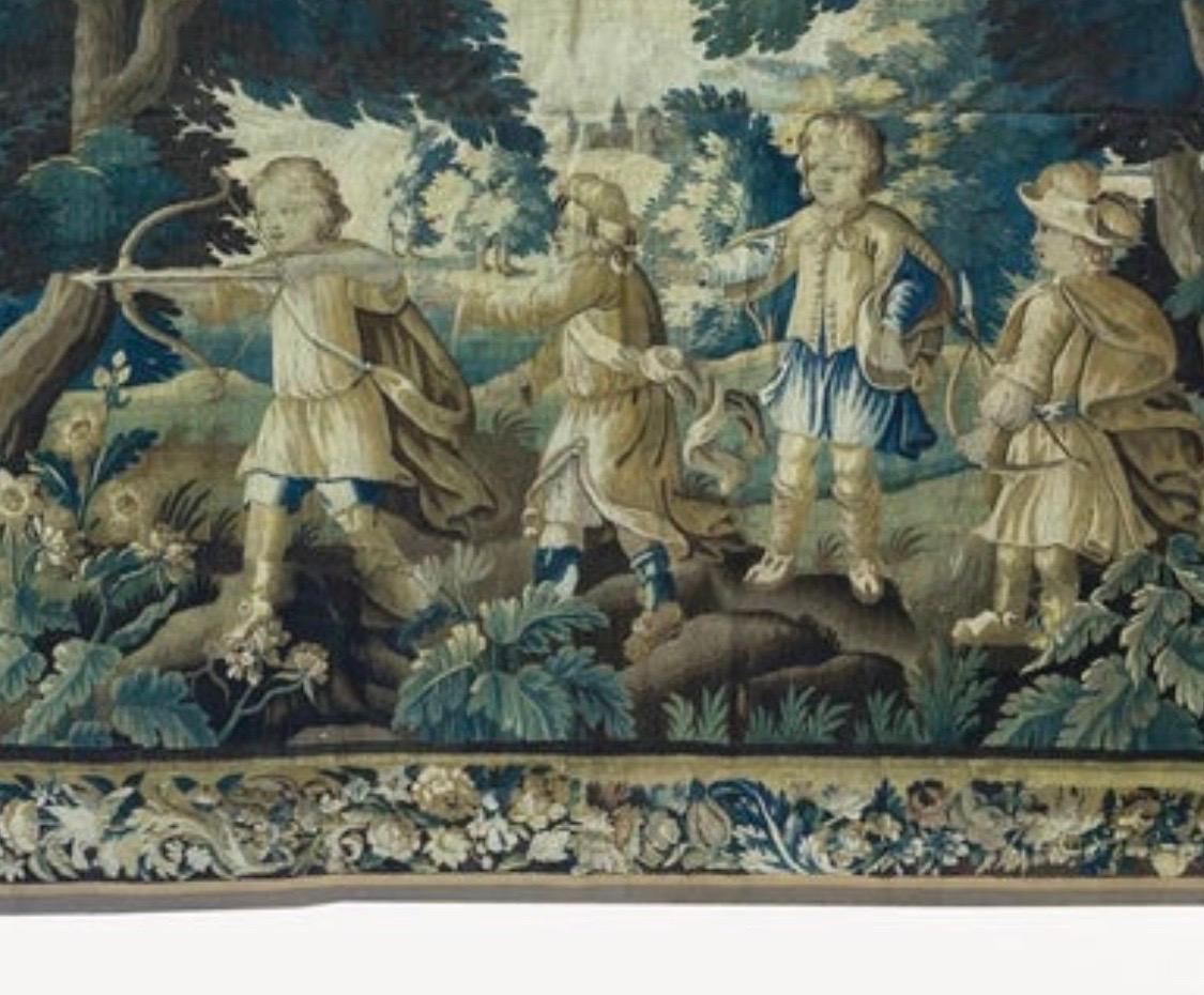 Il s'agit d'une magnifique tapisserie de verdure flamande ancienne du 17e siècle représentant des enfants nobles jouant dans les bois. La pièce se déroule dans une scène magnifique et riche d'une campagne aux arbres et à la végétation luxuriants. Il