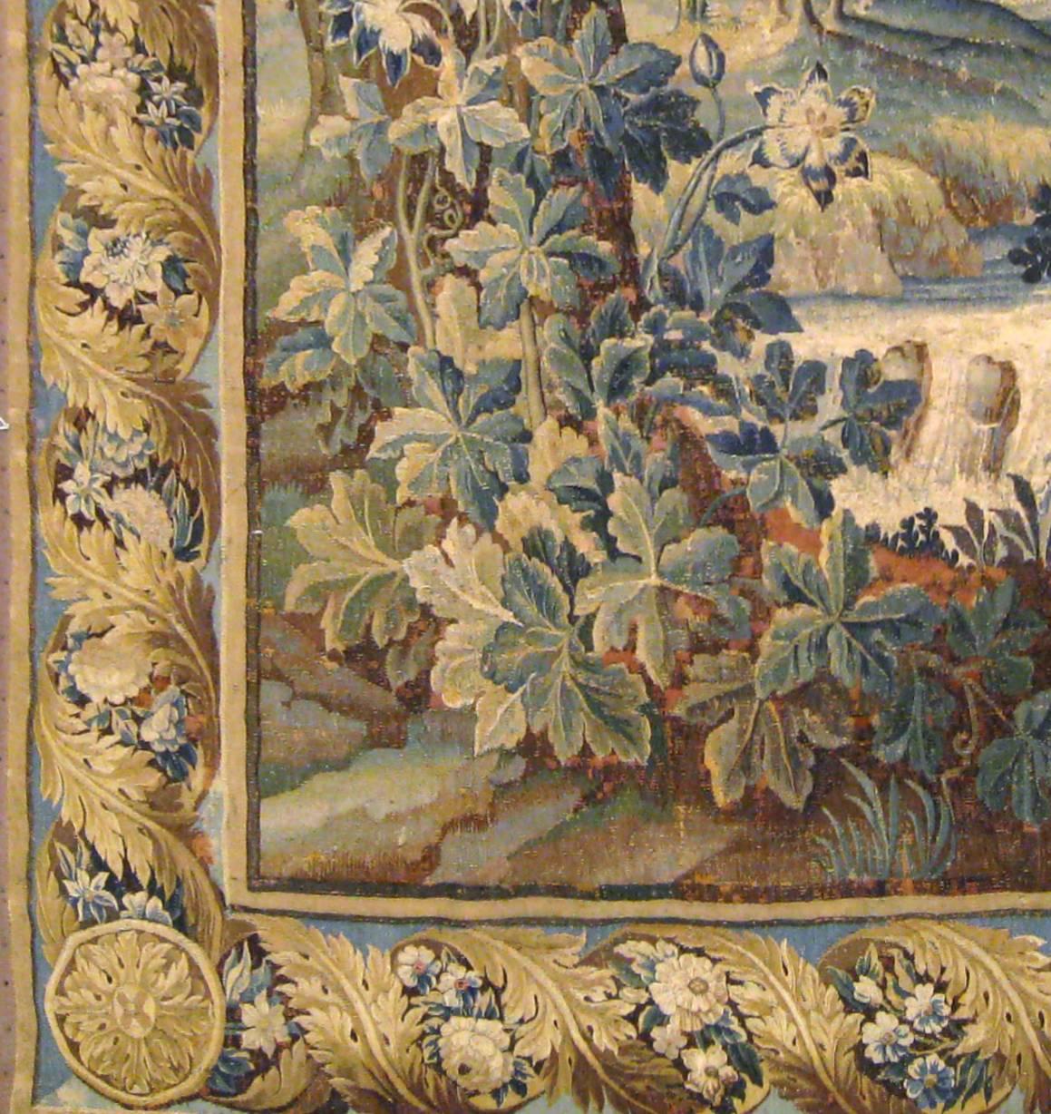 An antique 17th century Flemish verdure landscape tapestry, vertically oriented, size 9'4 H x 5'7 W. This handwoven tapestry depicts a pair of exotic birds in a tranquil verdant landscape, with one standing by a stream in the greenery at bottom