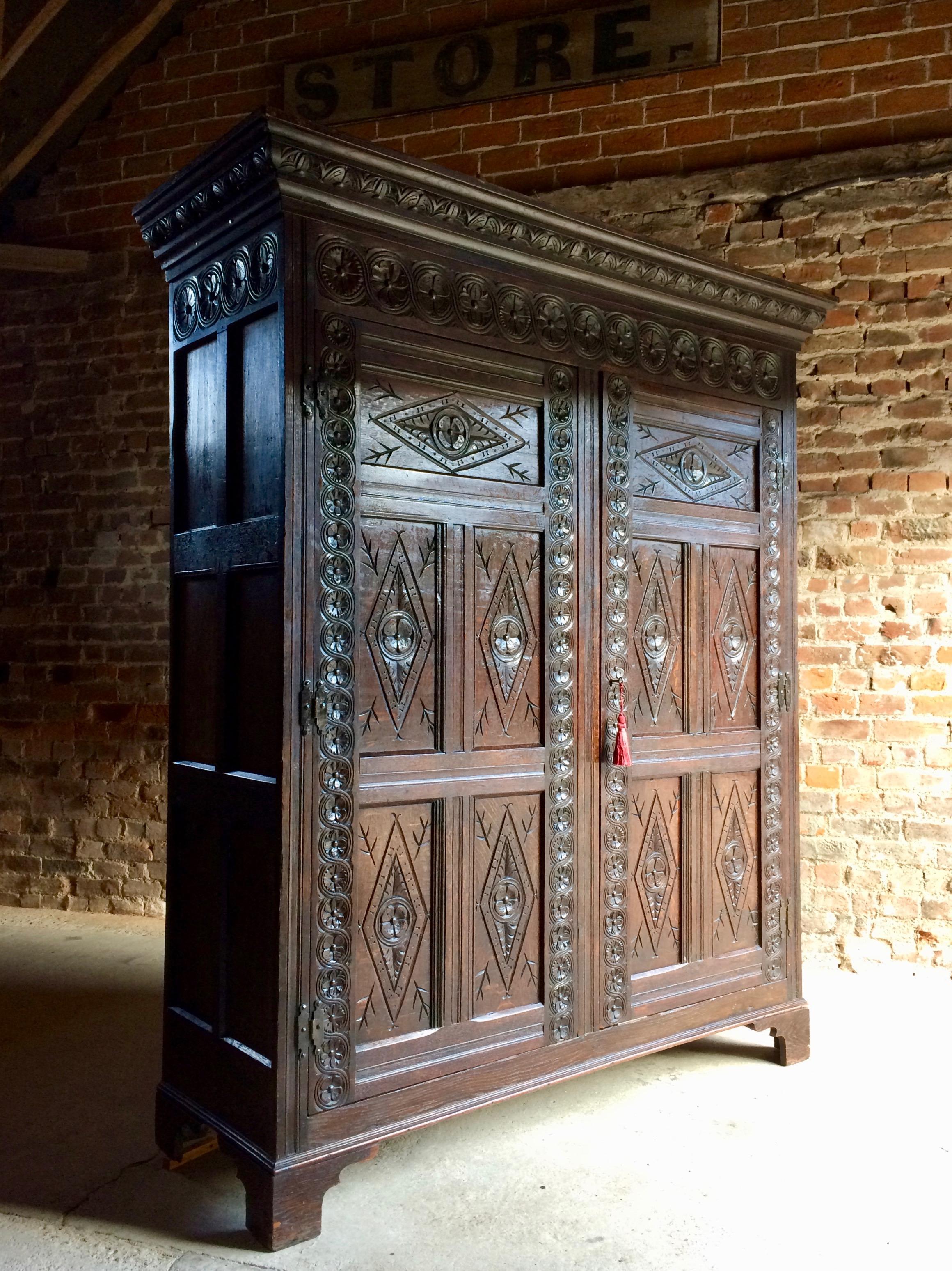 A magnificent antique 17th century style solid English oak heavily carved livery or hall cupboard circa 1790, the rectangular carved cornice top above two heavily carved panel cupboard doors with original iron butterfly hinges supported by rose head
