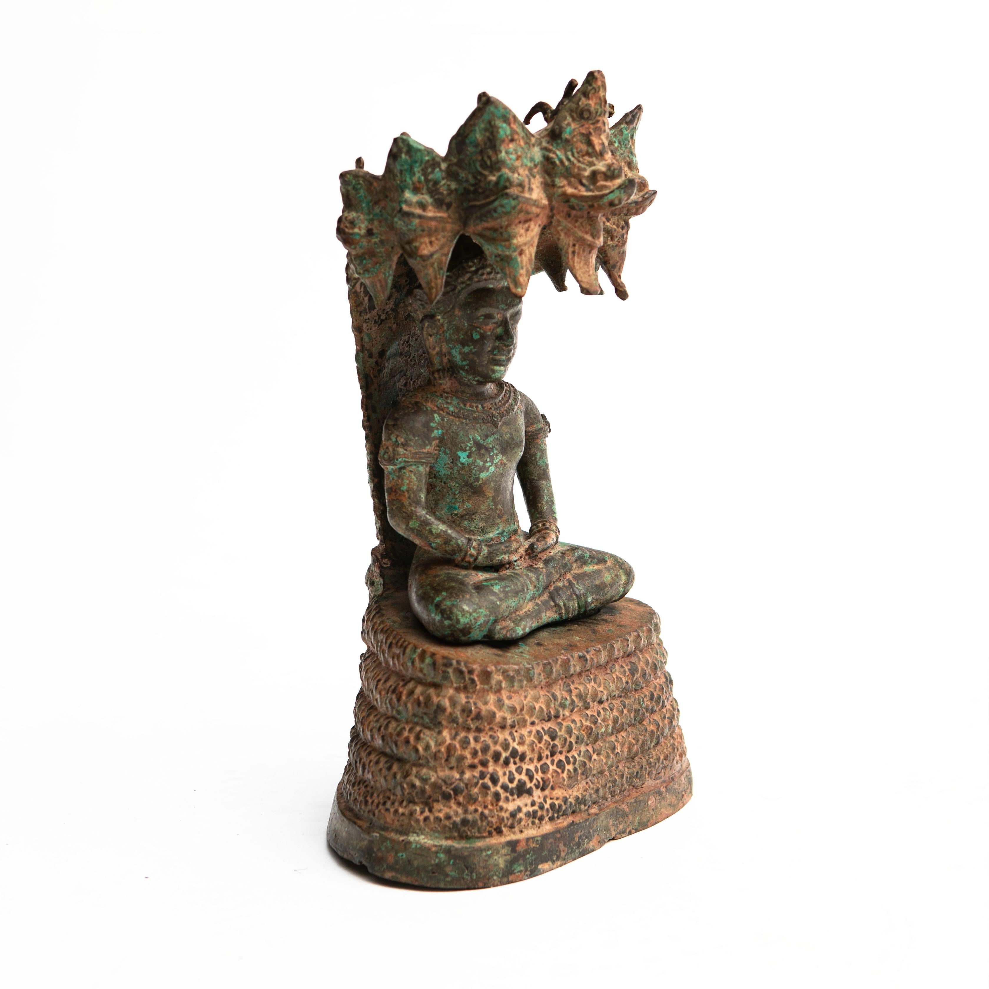 Bronze Buddha depicted in meditation pose sheltered by a Naga (a seven-headed snake). I two parts.
Naga's body coiled up to serve as a cushion for the Buddha with 7 pronged head providing a hood over the Buddha's head as a cover. Original condition