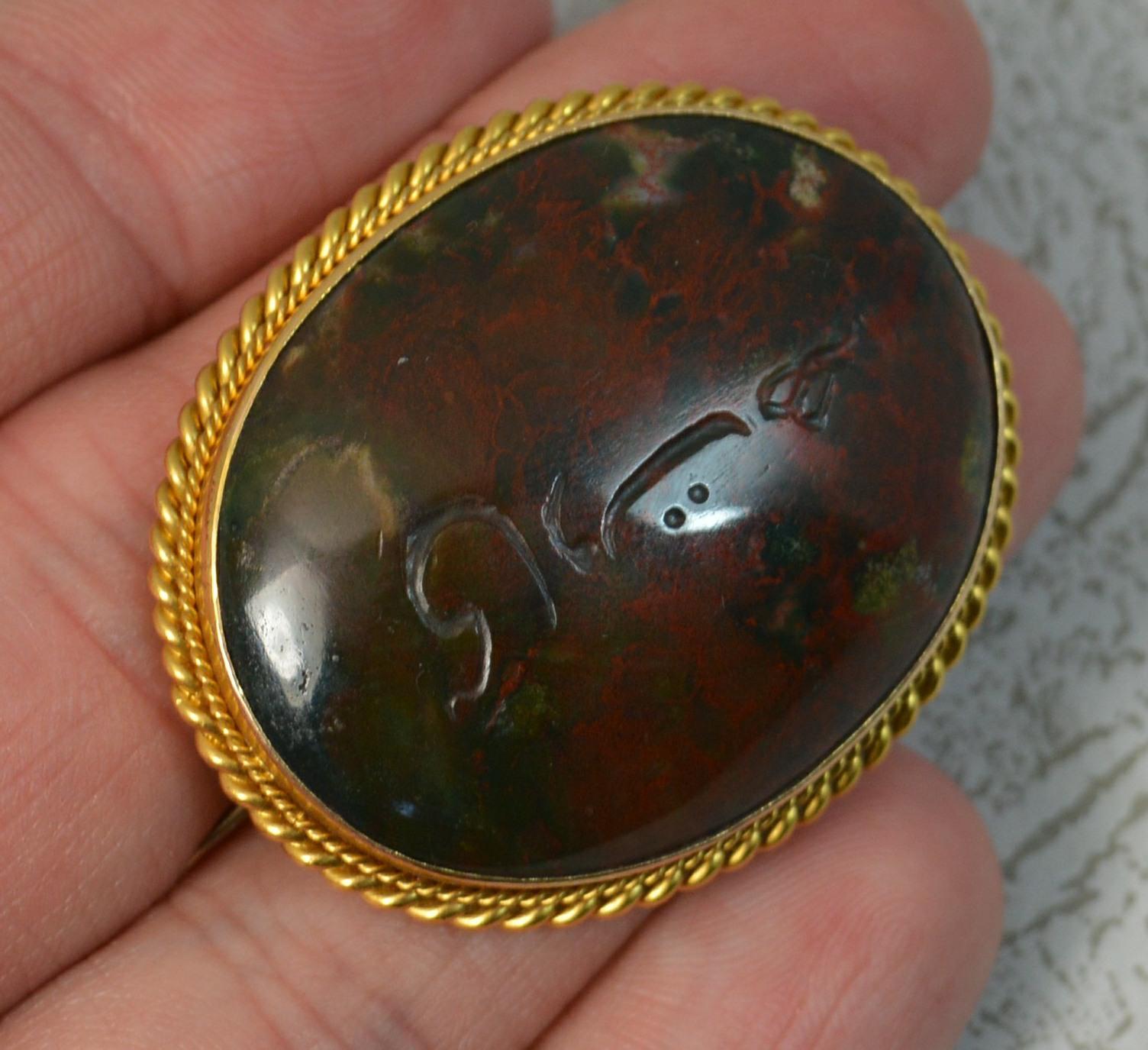 A large and bold antique brooch.
Solid 18 carat yellow gold border with rope twist edge.
Designed with a single oval bloodstone, full of reds, hand engraved writing.
37mm x 30mm approx. 14.2 grams.
Condition ; Good for age. Well set stone, issue