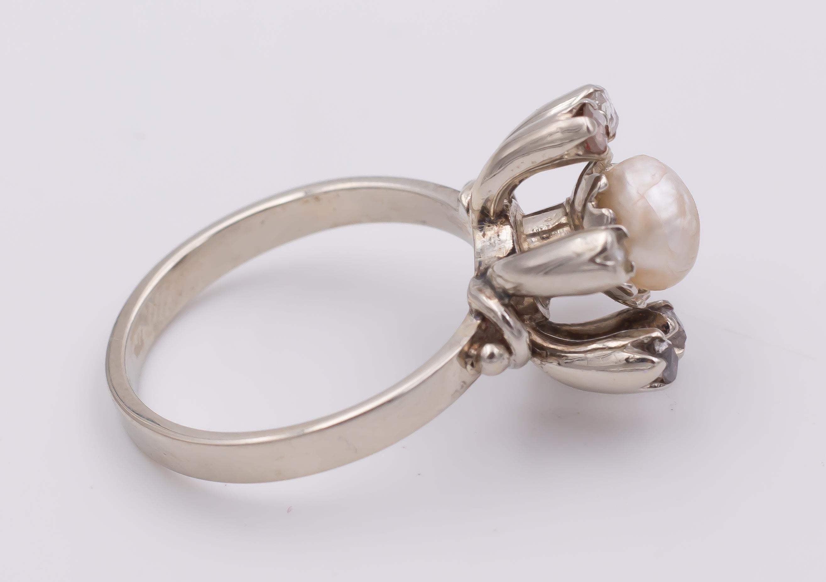 This fine and elegant ring has a beautiful flower shape: it is set with a central pearl, surrounded by six petals, the rose cut diamonds in a gold mount.
The ring is crafted in white gold throughout and dates from the 1930s. 

MATERIALS
White gold,