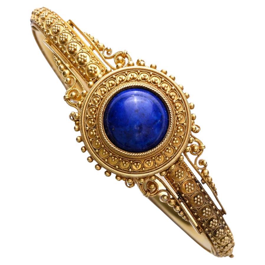 18K yellow gold, opening rigid bead bracelet set with a tinted lapis lazuli cabochon in a twisted closed setting, in a granulated and filigree decor, with a ratchet clasp with safety chain.
Mid-19th century, probably Italian.
Gross weight: 16.50