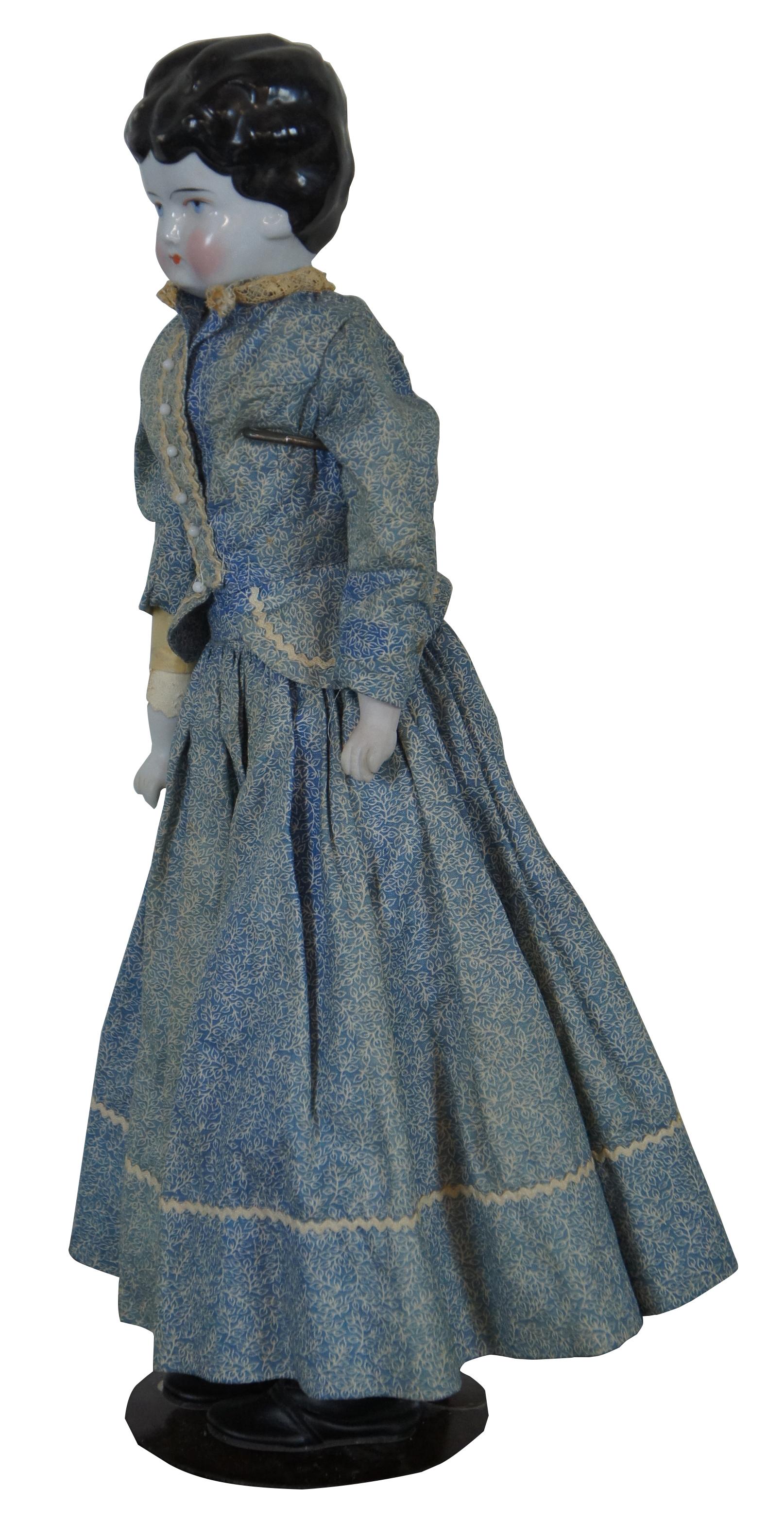 Antique china doll with black hair and blue eyes, dressed in a blue Victorian outfit; head and hands are porcelain, body is leather, circa 1850.
 