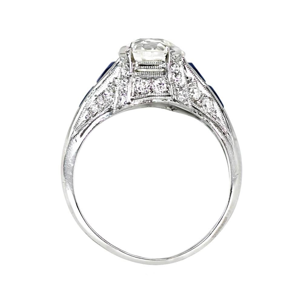 An Art Deco era antique engagement ring holds a 1.85 carat old European cut diamond in prongs, with J color and VS1 clarity. Two French cut natural sapphires are set east-west on the shoulders with a combined weight of 0.20 carats. The platinum