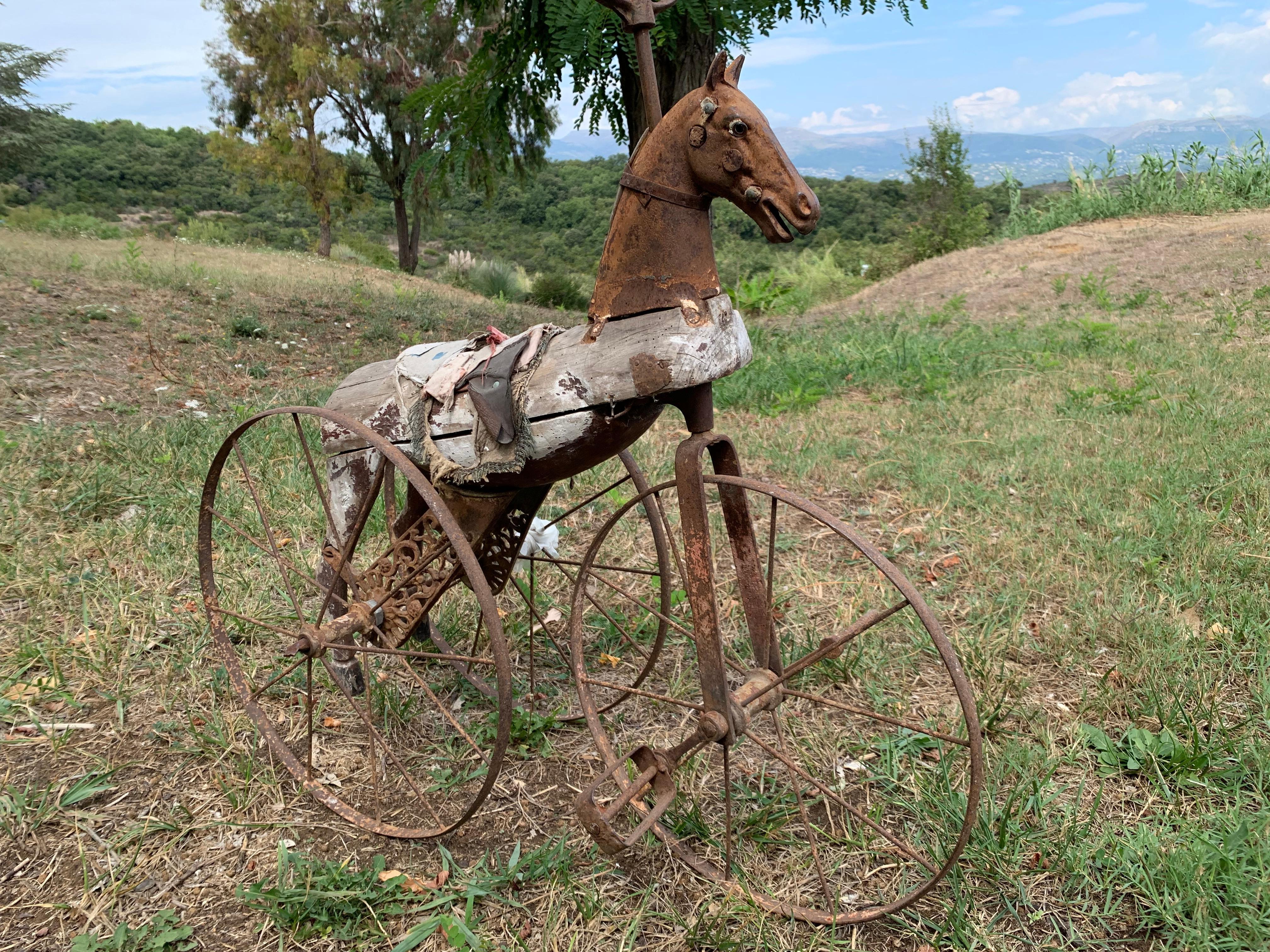 This quite amazing children's tricycle has seen it's best days along time ago, however it has retained all it's charm and magic.
The face, the handles and the wheels are made out of rusty metal. The body is carved out of wood, still covered with
