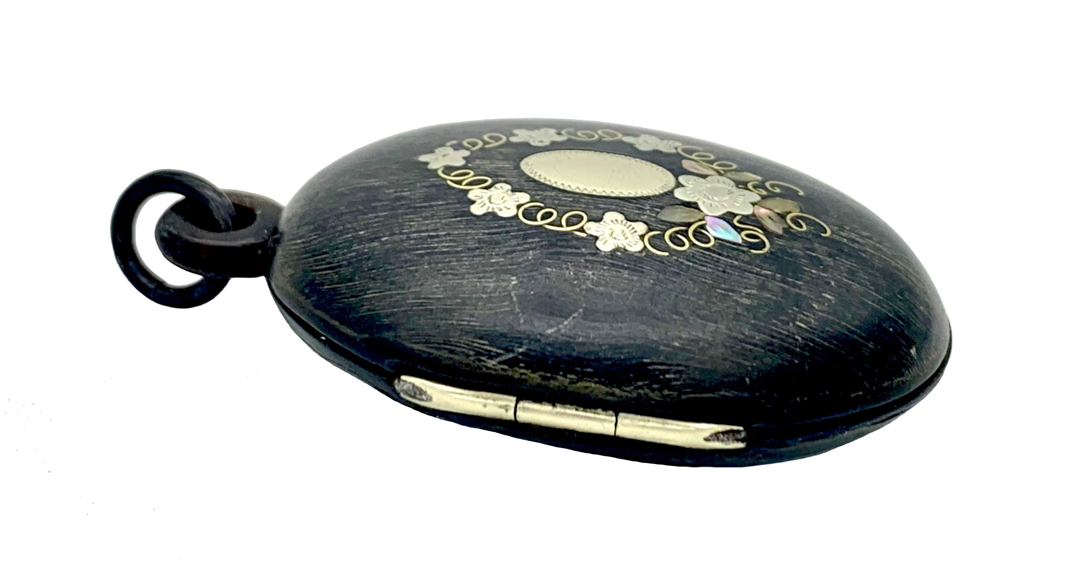 This good size locket has been handcrafted around 1880 out of horn. The front shows fine lines typical for horn. Surrounded by fine lines the locket has been decorated with a flower wreath and an oval plaque. The design is executed in fine inlay