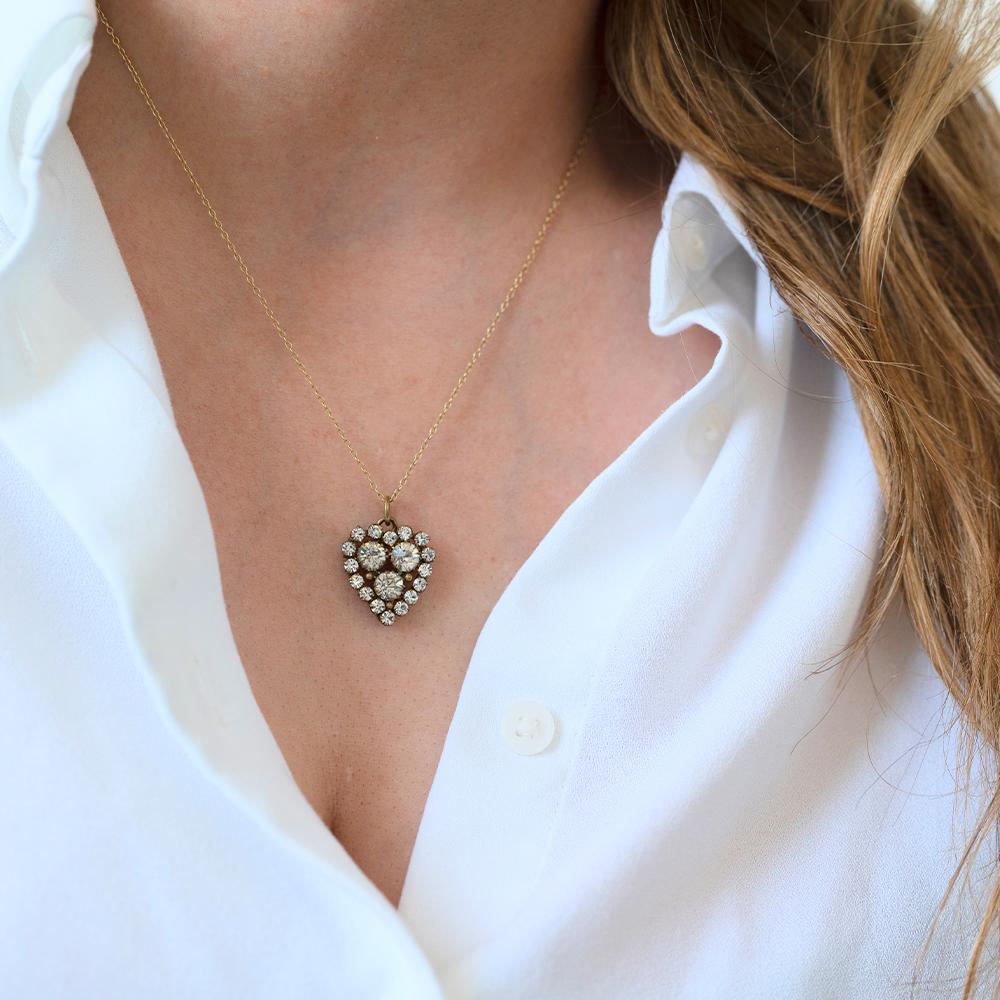 This exquisite Victorian heart pendant is set with three larger clear paste stones surrounded by a halo of smaller pastes, all beautifully mounted in warm-toned brass. The stones are housed in closed-back settings, typical of the 19th century, which