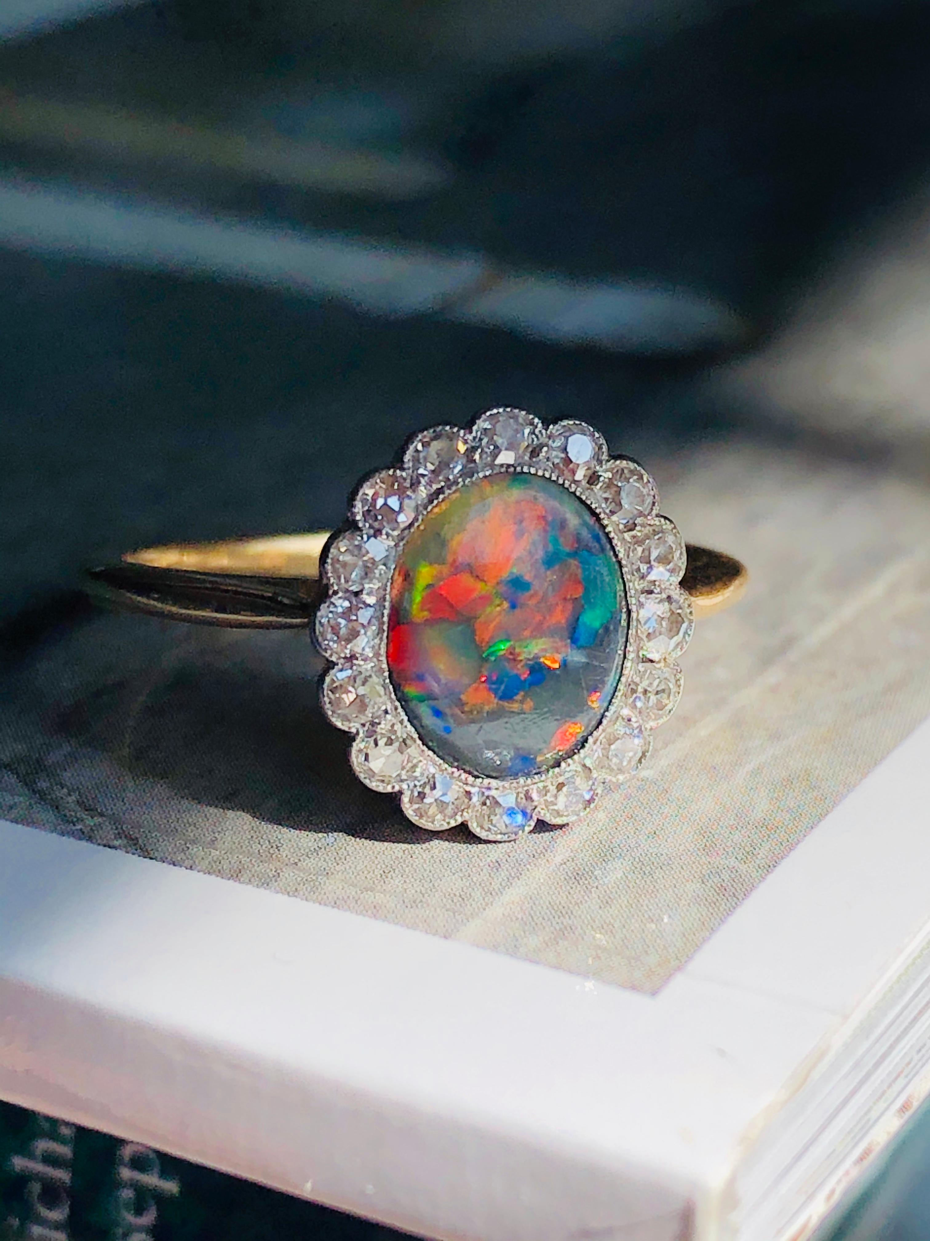 Black Opal and Diamond Ring. Collet-set with an oval black opal, displaying a superb play of colour against a dark grey background. Opal iridescence is caused by light interacting with an extremely fine network of silicon dioxide spheres within the