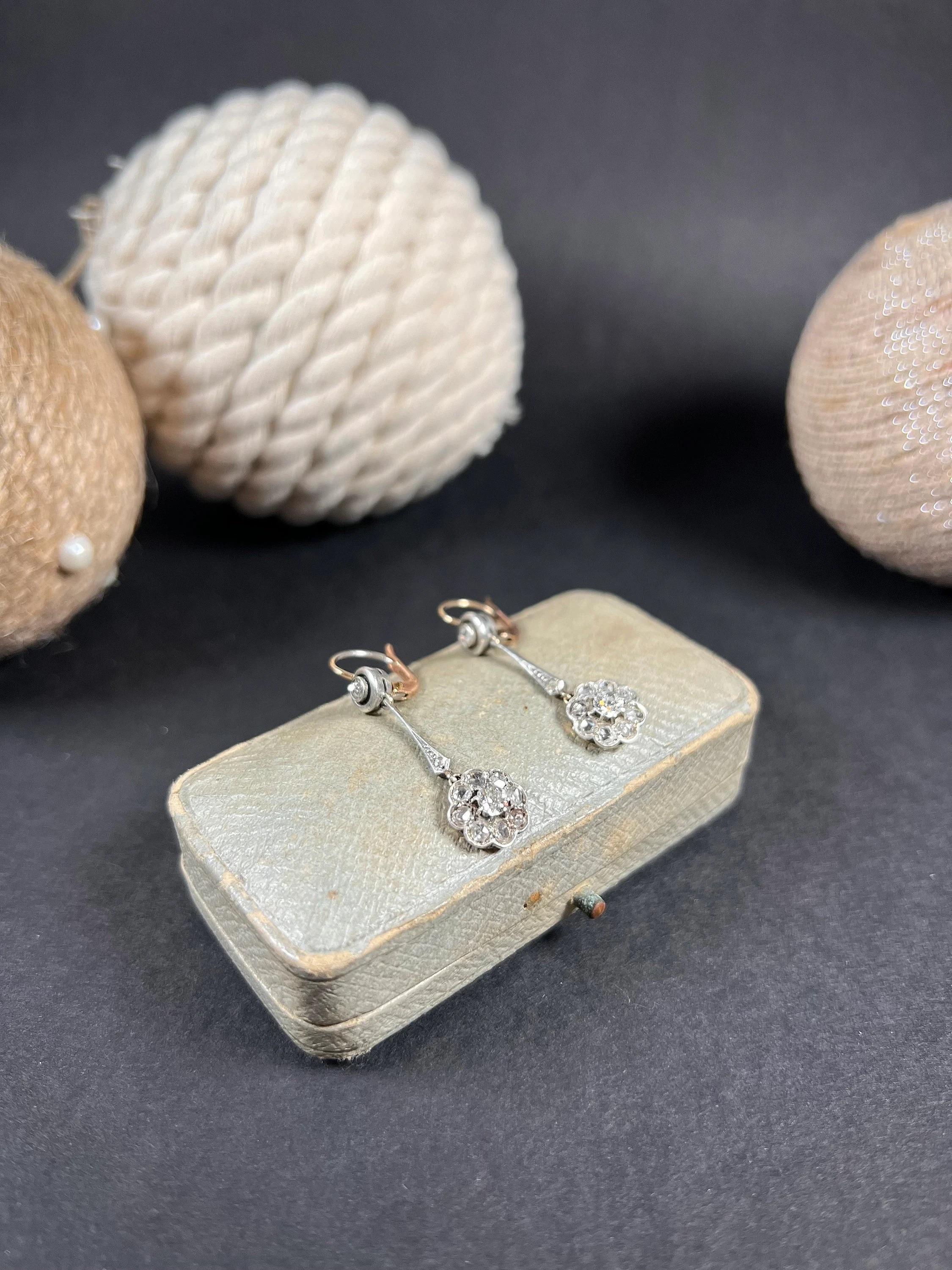 Antique Diamond Earrings 

18ct Yellow Gold & Platinum Tested

Circa 1900

These stunning drop-style earrings exude a classic charm with their elegant long stems and diamond-set daisy formations at the bottom. The earrings boast a sophisticated