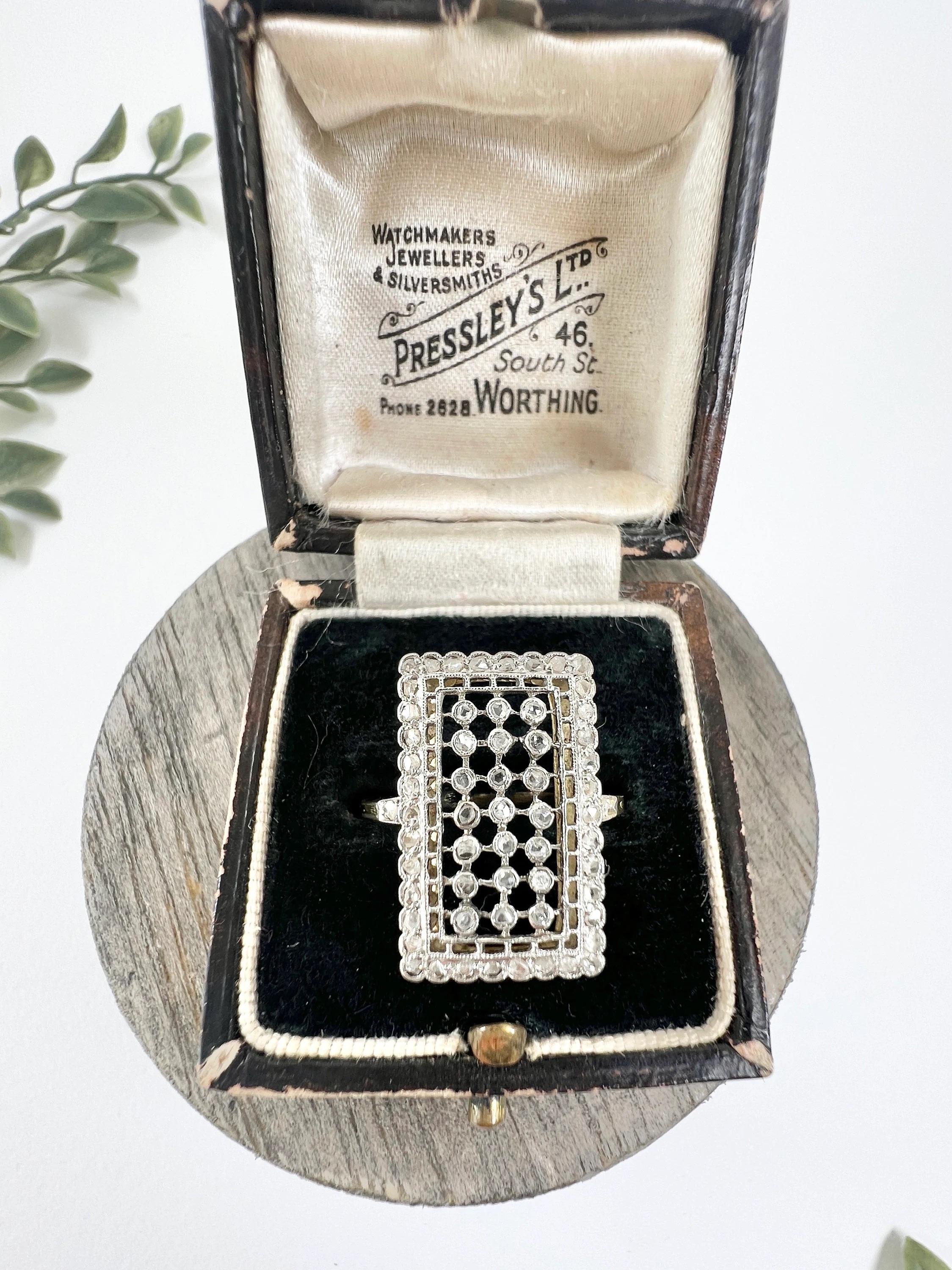 Antique Diamond Ring

18ct Gold & Platinum Tested

Circa 1910

Introducing a stunning Edwardian-era ring, crafted from 18ct gold and platinum. This exquisite piece features a rectangular-shaped, open-work, plaque-style design, adorned with