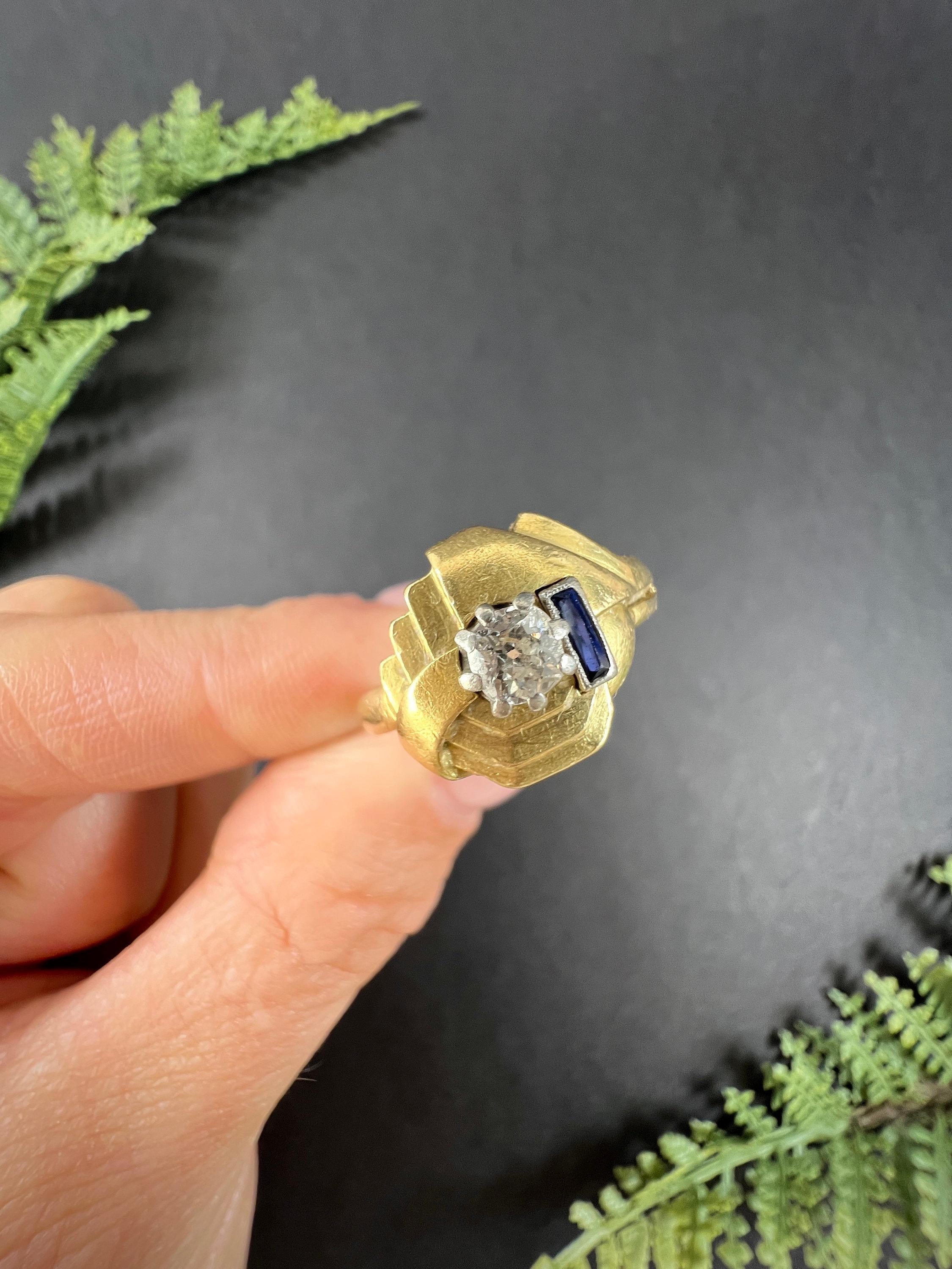 Gold Art Deco Ring 

18ct Gold Stamped 

Circa 1920s

Elevate your style with this exquisite 18ct yellow gold art deco ring boasting a captivating tiered geometric design adorned with a stunning French cut sapphire and an old European cut diamond,