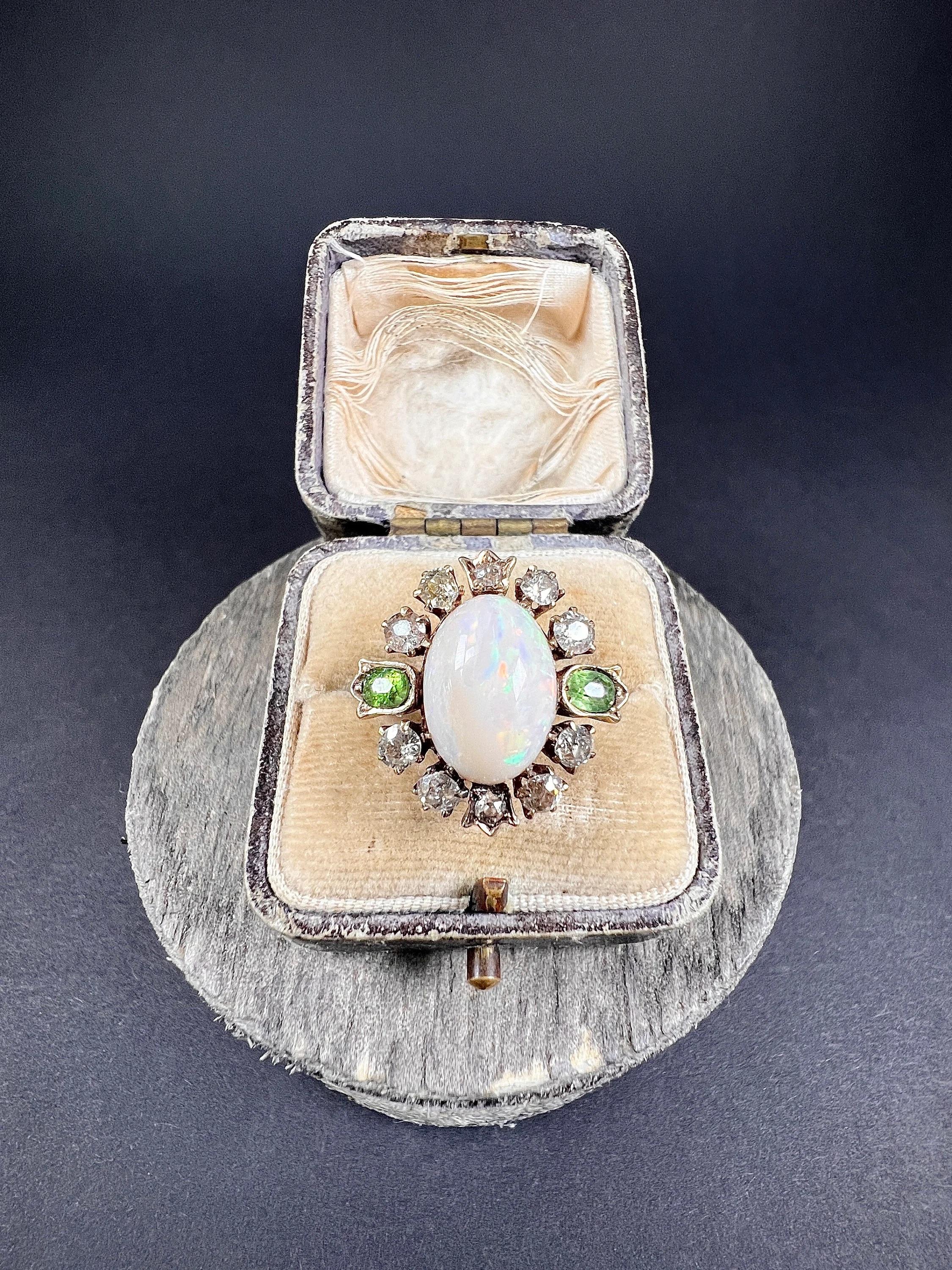 Antique Opal Cluster Ring 

18ct Gold Tested

Circa 1880

Introducing a stunning Victorian 18ct gold cluster ring, featuring a magnificent opal at its centre surrounded by a cluster of natural diamonds and two demantoid garnets in tulip settings.