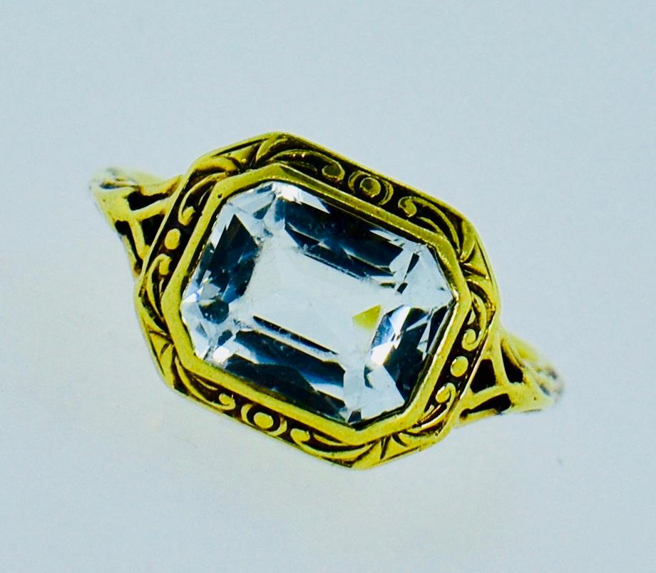 18K and Aquamarine antique ring. The center emerald cut Aquamarine measures 9.79 by 6 mm.  It is a clean stone with a light blue color.  The filigree gold work is done well.  The natural stone does have some slight abrasion as seen under a