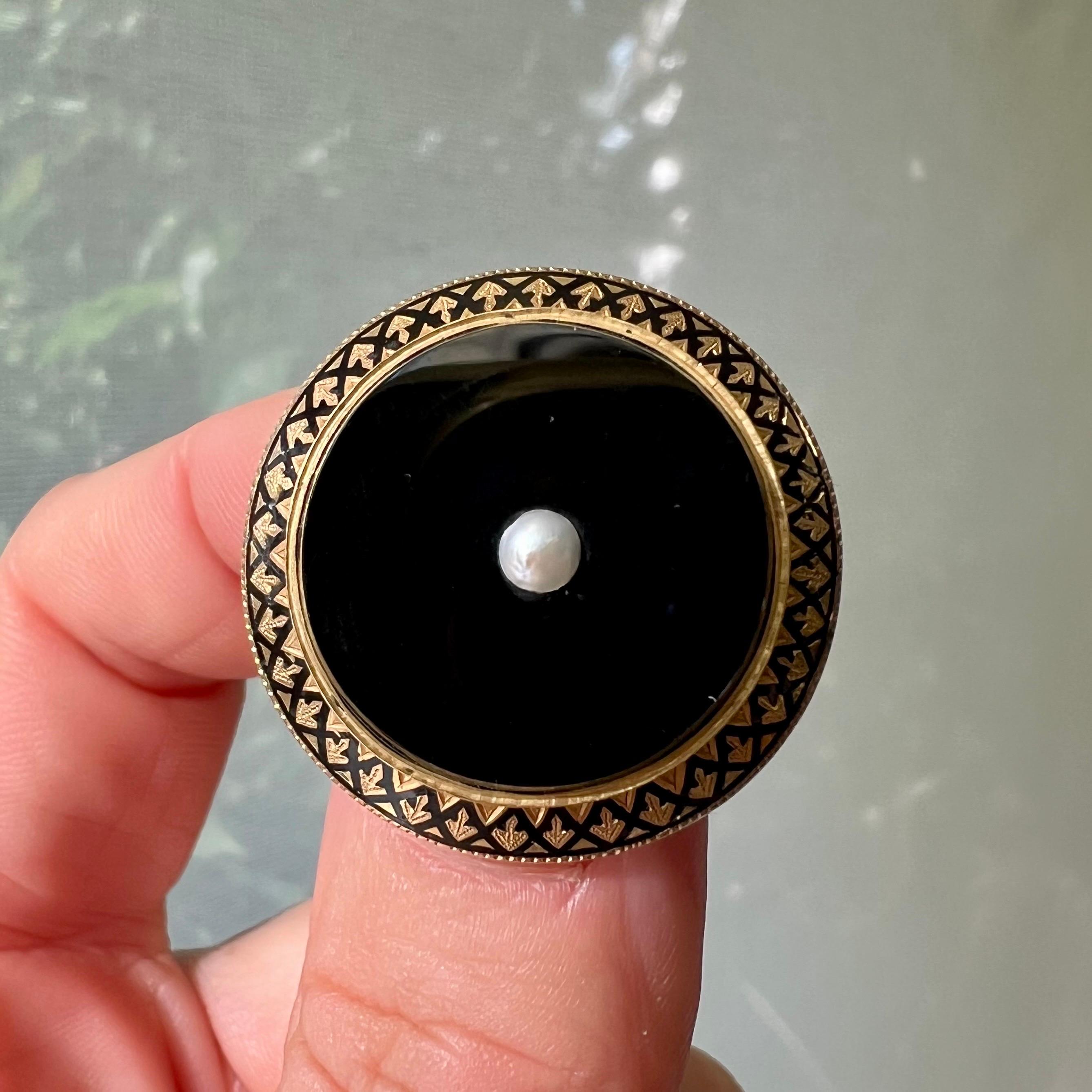 This antique 18 karat gold and enamel round brooch is created with black onyx and set with a seed pearl in the center. The border of the brooch is decorated with black enamel and a gold twisted rim. The pin at the back of the brooch is provided with
