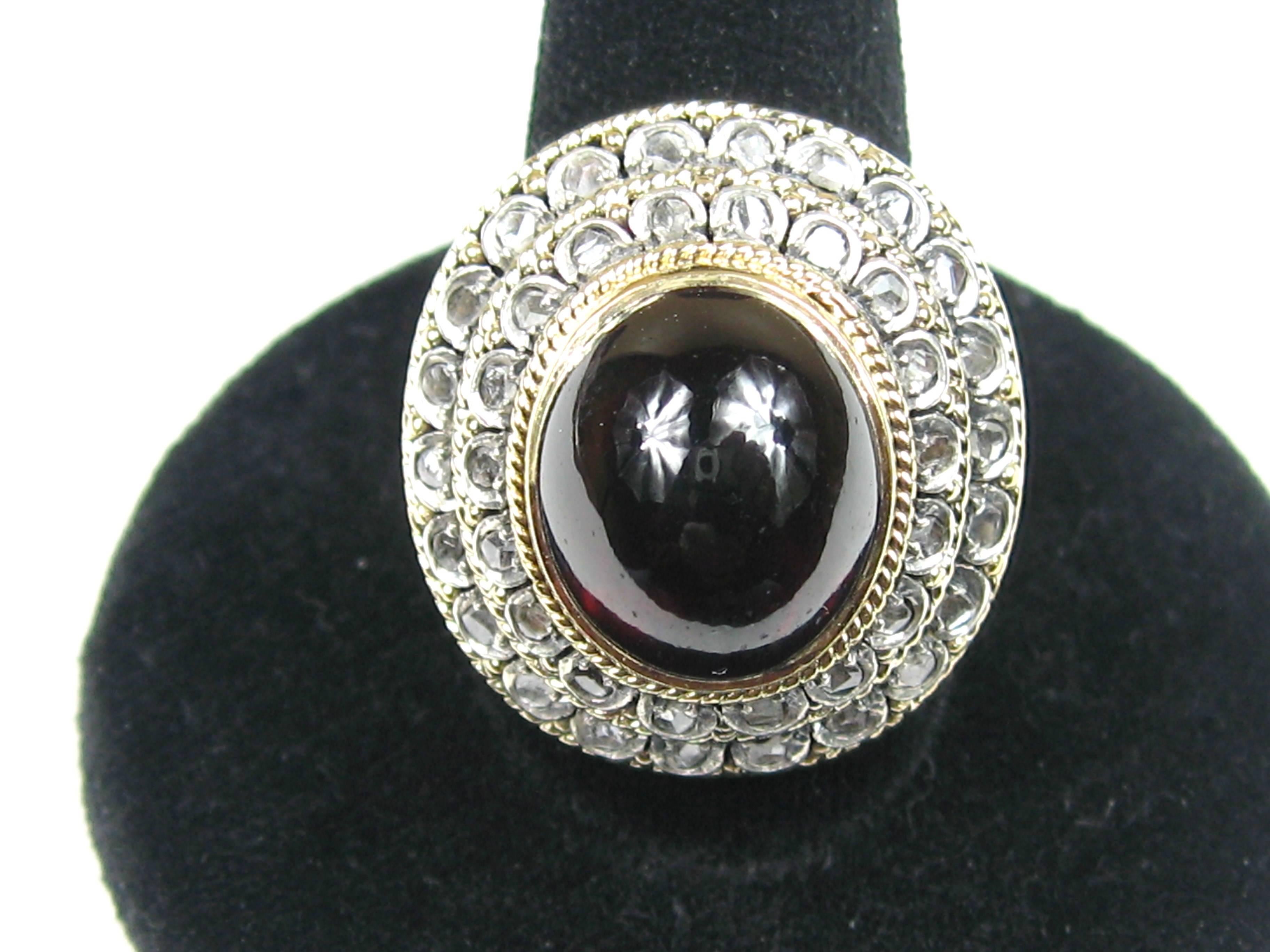 A Spectacular 18K Gold Garnet Ring. Large Cabochon Garnet center with 2 tiers of mine cut diamonds surrounding. The shank has elaborate cuts. The underside of the ring is decorated as well, this is a spectacular piece! The Diamonds are set in White