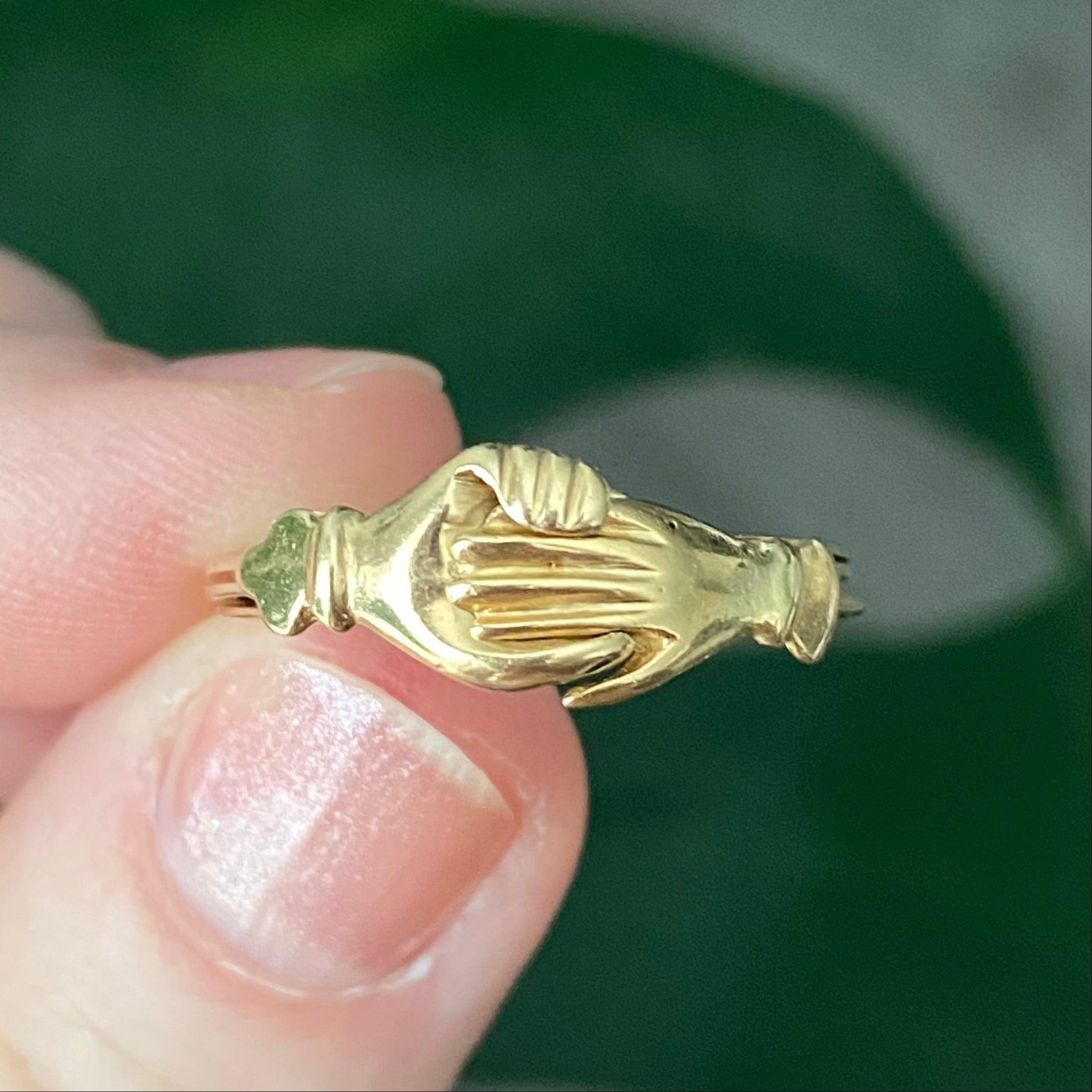 Dreifach-Ring aus 18 Karat Gelbgold mit drei Teilen, die durch eine Niete auf der Rückseite verbunden sind. Die beiden Hände greifen ineinander und öffnen sich dann, um ein darunter verborgenes Herz zu enthüllen. 
Als Symbol für die Vereinigung
