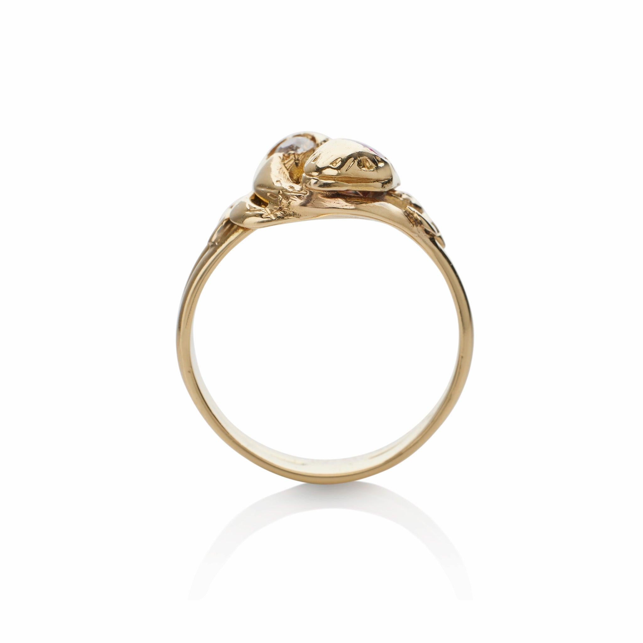 This late Victorian 18K gold double snake ring, set with a diamond and a ruby, was created in England in 1892. It is designed as two engraved snake heads, each with an old European-cut diamond or a circular-cut ruby, completed by their intertwined