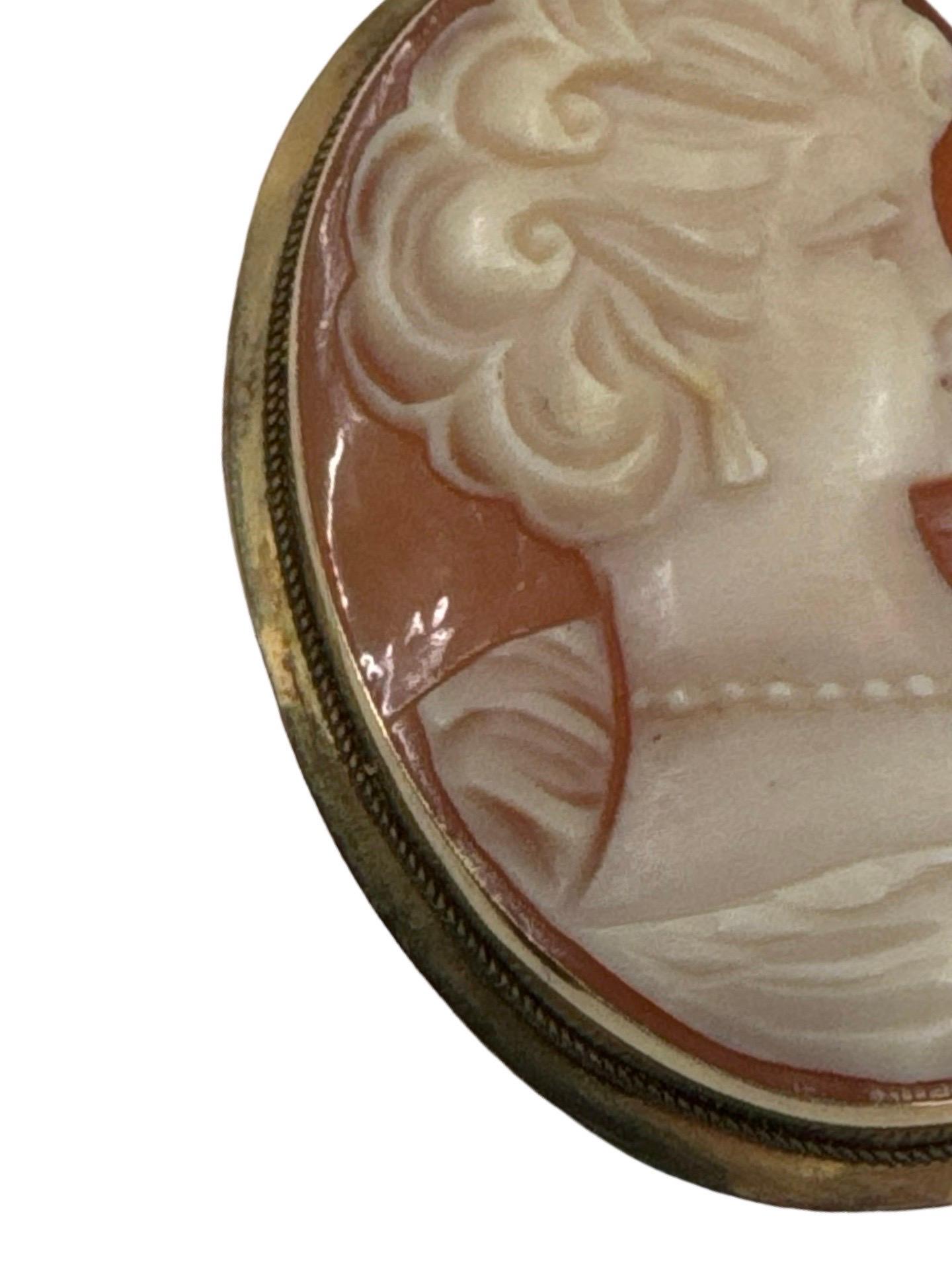 Refinado colgante camafeo antiguo, tallado a mano en concha natural con un retrato en altorrelieve de una dama clásica de perfil. La pieza presenta un detallado marco de oro amarillo de 18 quilates con un fino bisel de cuerda y dos enganches para