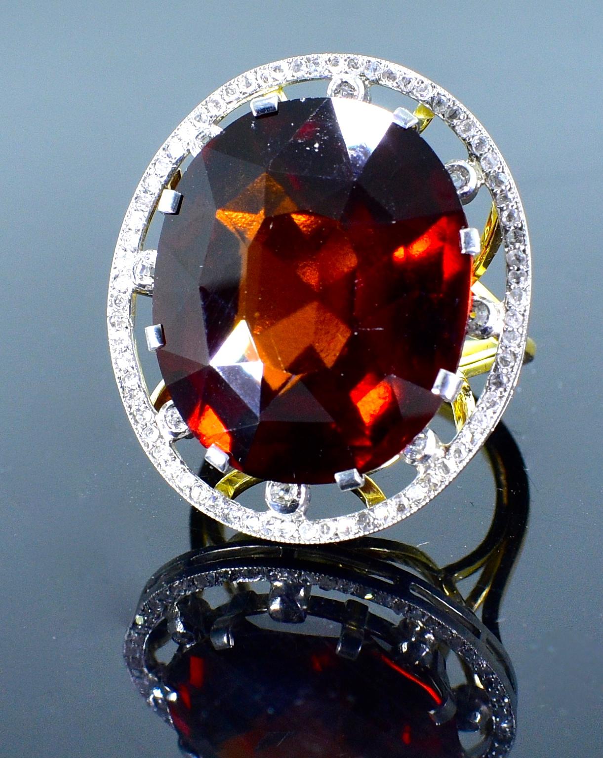 Antique ring centering a fine and unusual orange garnet weighing 26 cts., and displaying a fine deep orange/red color.  Surrounding this antique cushion cut stone are rose cut and European cut diamonds.  This ring is in fine condition and a size