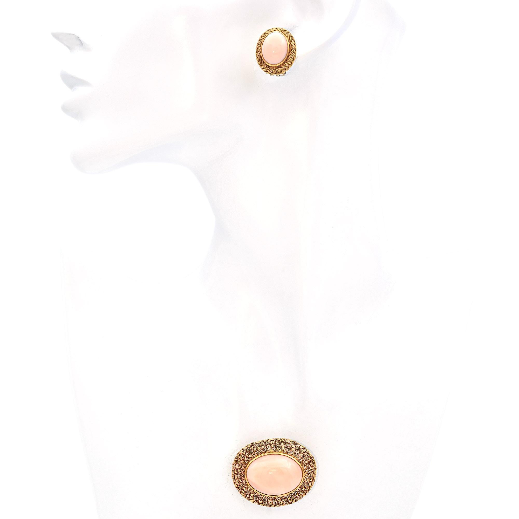 This exquisite jewelry set features a brooch and matching earrings, each adorned with a smooth, oval orange coral stone. The coral is encased in intricately woven 18k gold, creating a stunning contrast and highlighting the stone's natural beauty.