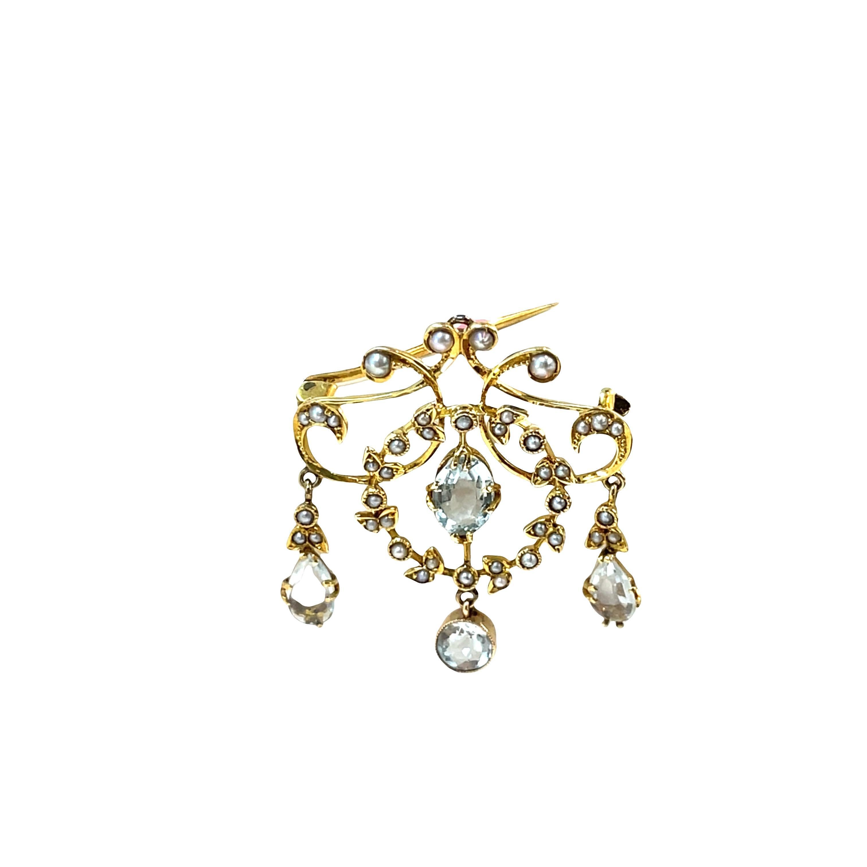 Rehaussez votre collection d'accessoires avec cette broche antique exquise, réalisée en luxueux or jaune 18 carats. Ornée de délicates perles de rocaille rondes et d'une superbe pierre précieuse aqua ovale, avec deux aquas poires et un aqua rond